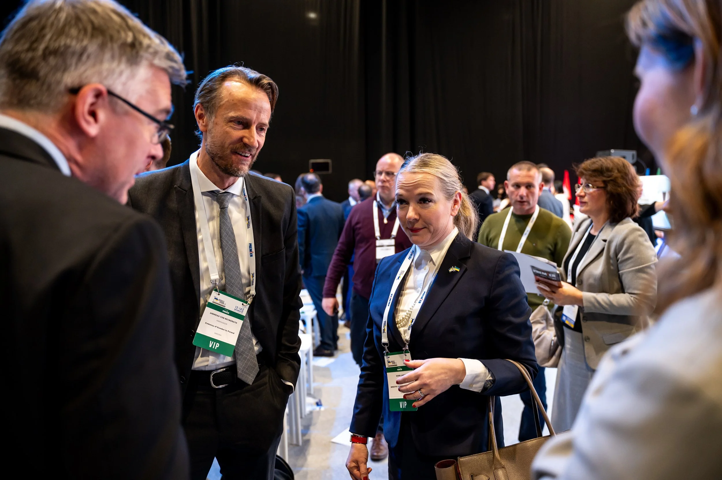Group of business professionals having a conversation at a conference, with many others in the background.
