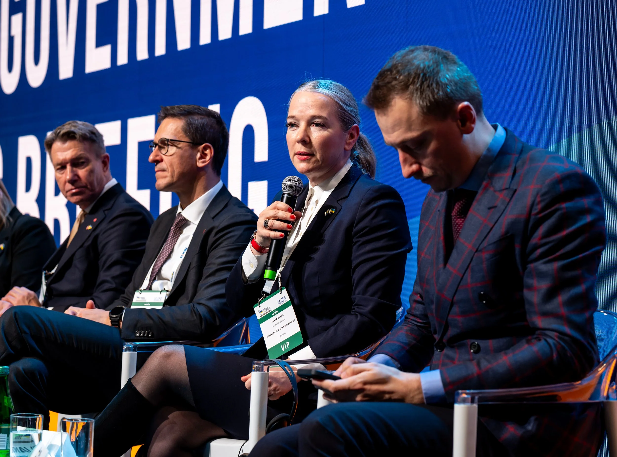 People sitting on a panel at a conference, with a blue background saying 'GOVERNMENT' and some other text that is partially visible.