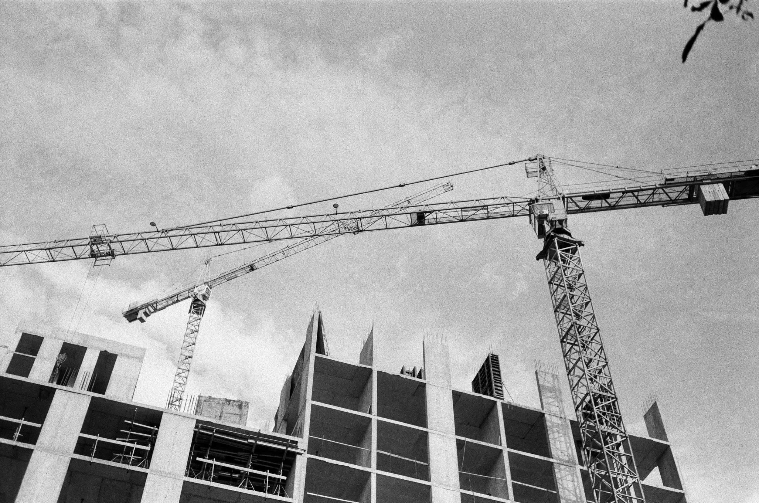 Black and white photo of a construction site with a large building under construction and a tall tower crane.