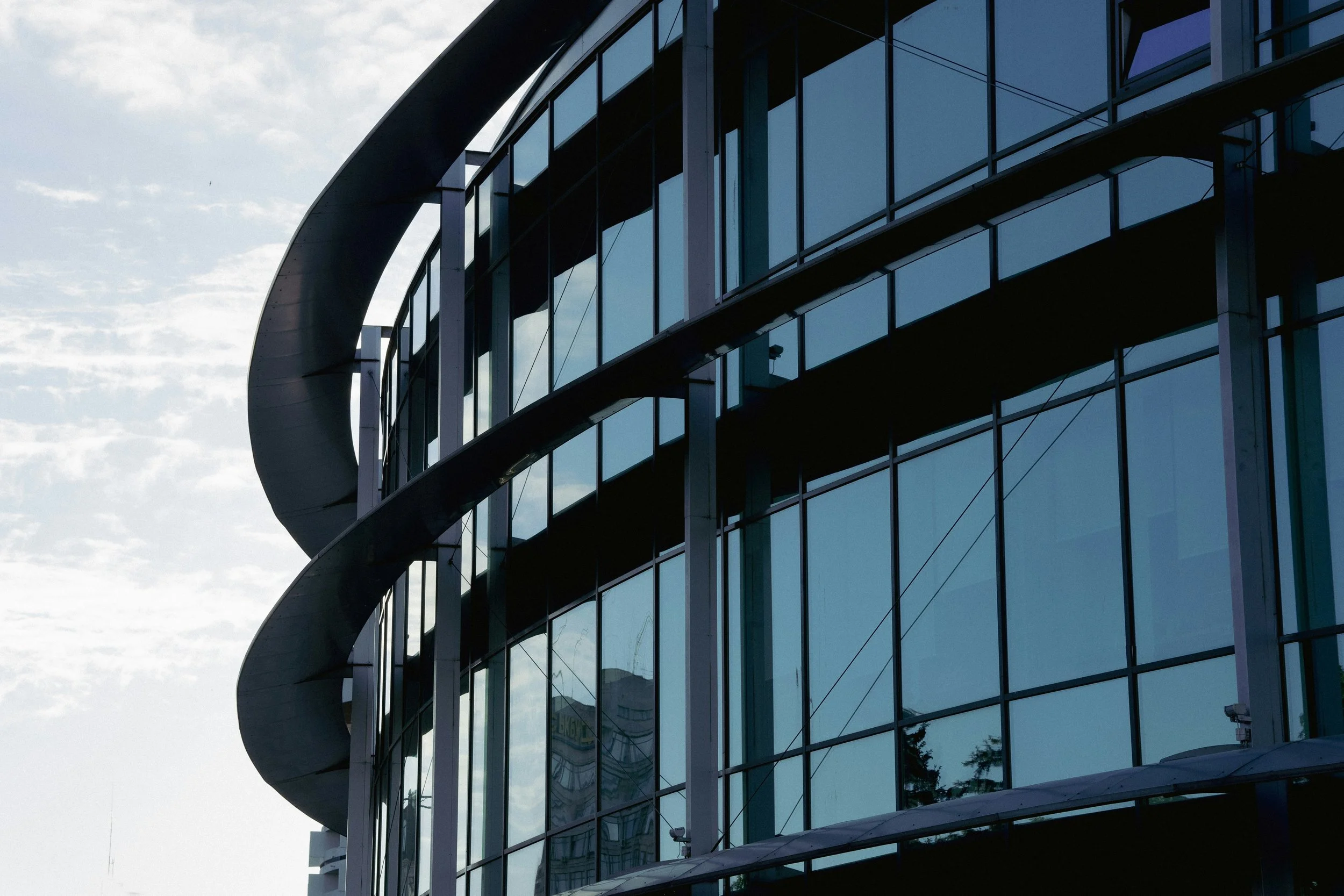 Close-up view of a modern glass building with curved metal accents and reflections of the sky.