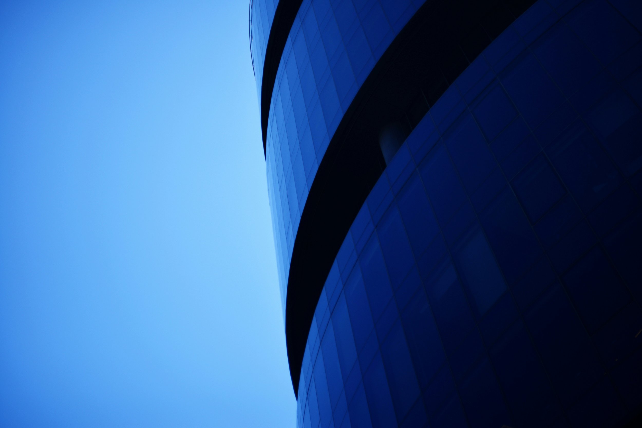 Close-up of a modern building with reflective glass windows and a curved corner, against a clear blue sky.