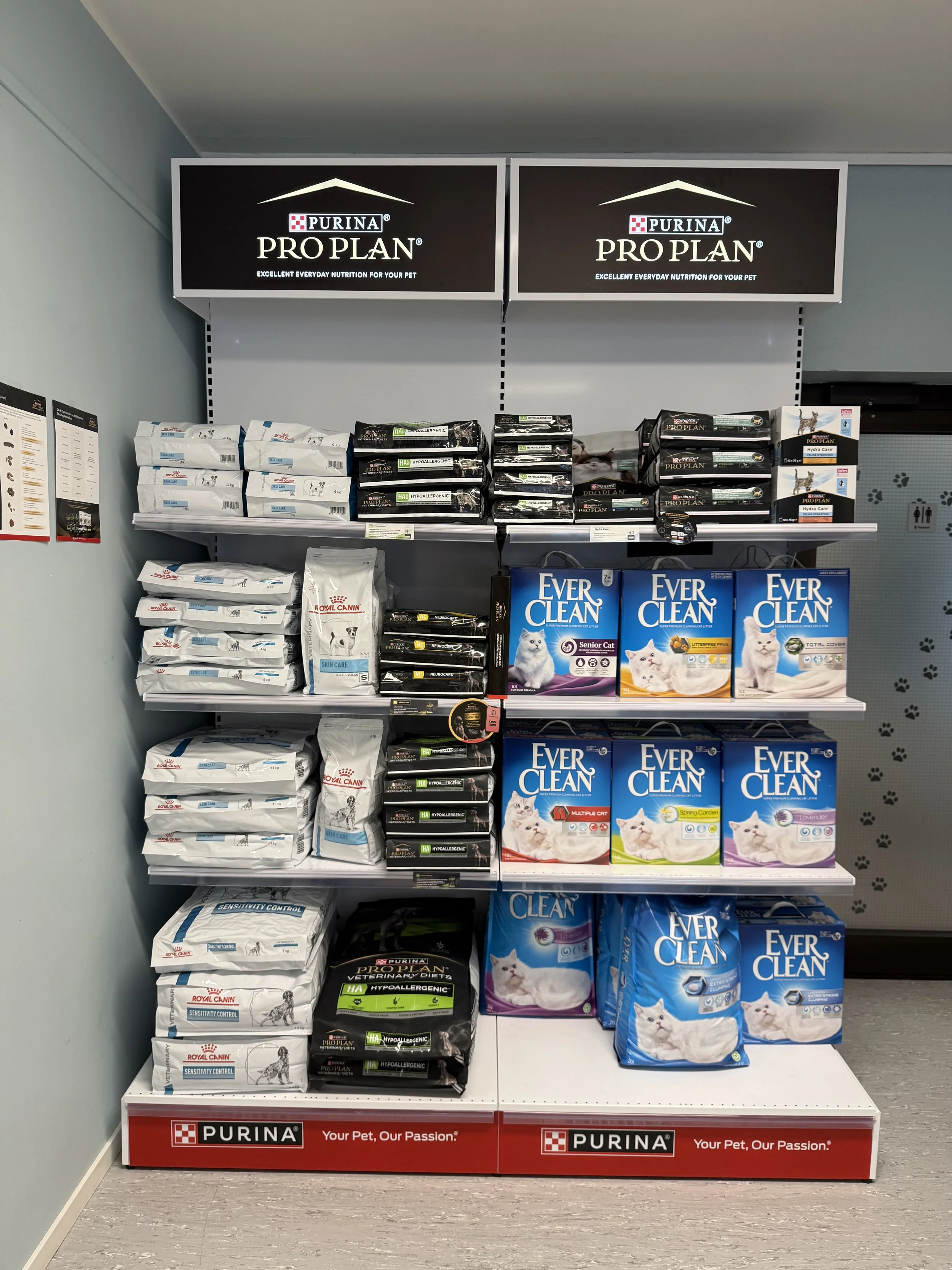Perspektivbilde av hyller med katte- og hundefôr, merker som Purina Pro Plan og Ever Clean, i en dyrebutikk.