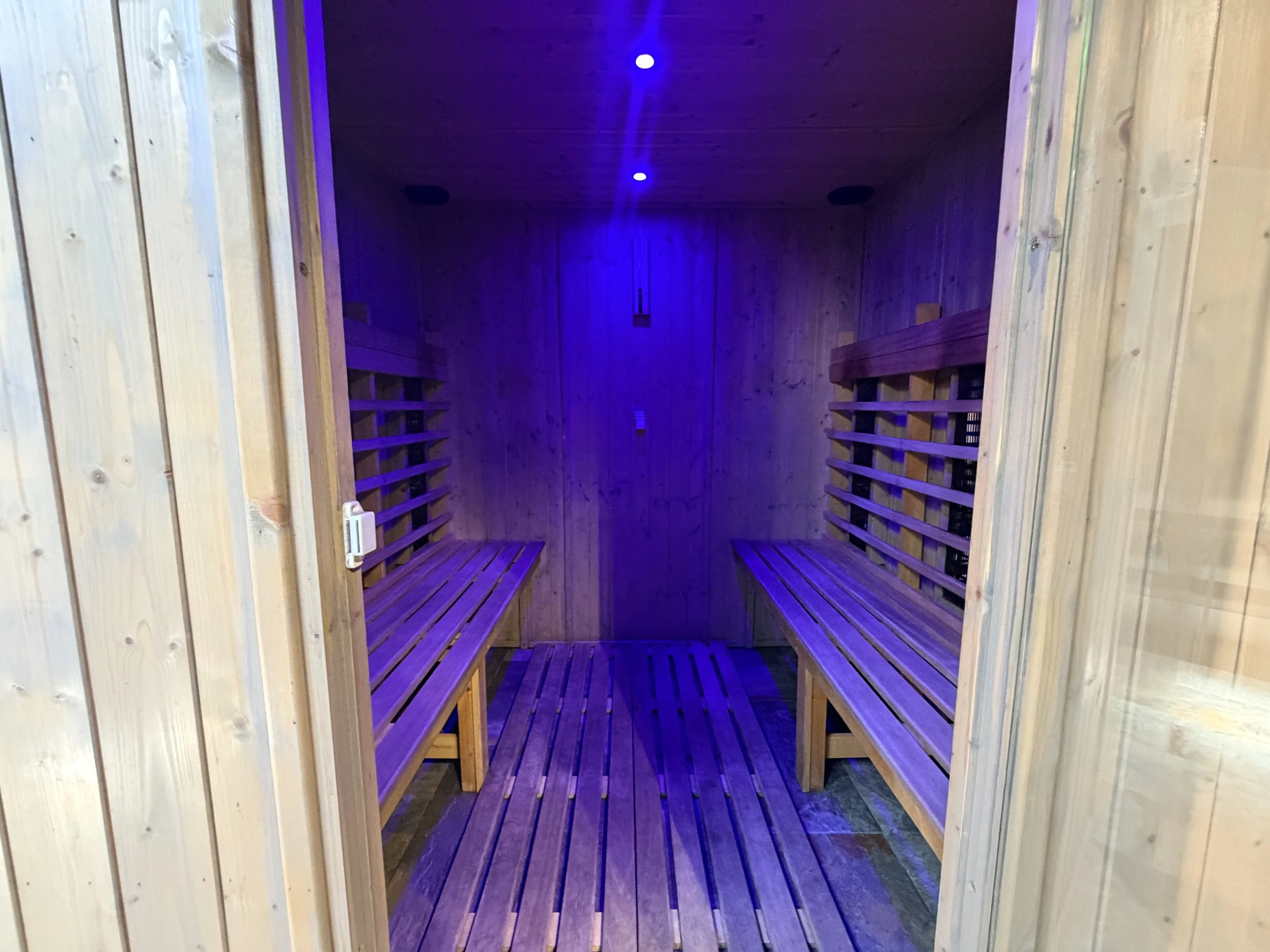 A wooden sauna room with benches on both sides and purple lighting overhead.