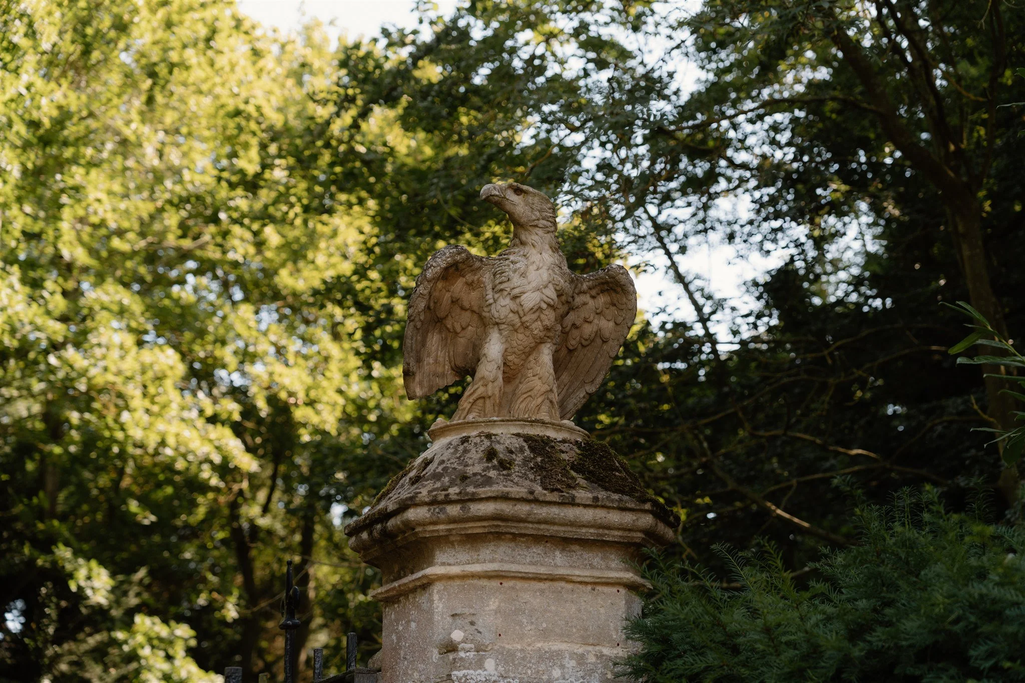 A stone eagle sculpture on a pedestal surrounded by greenery and trees.