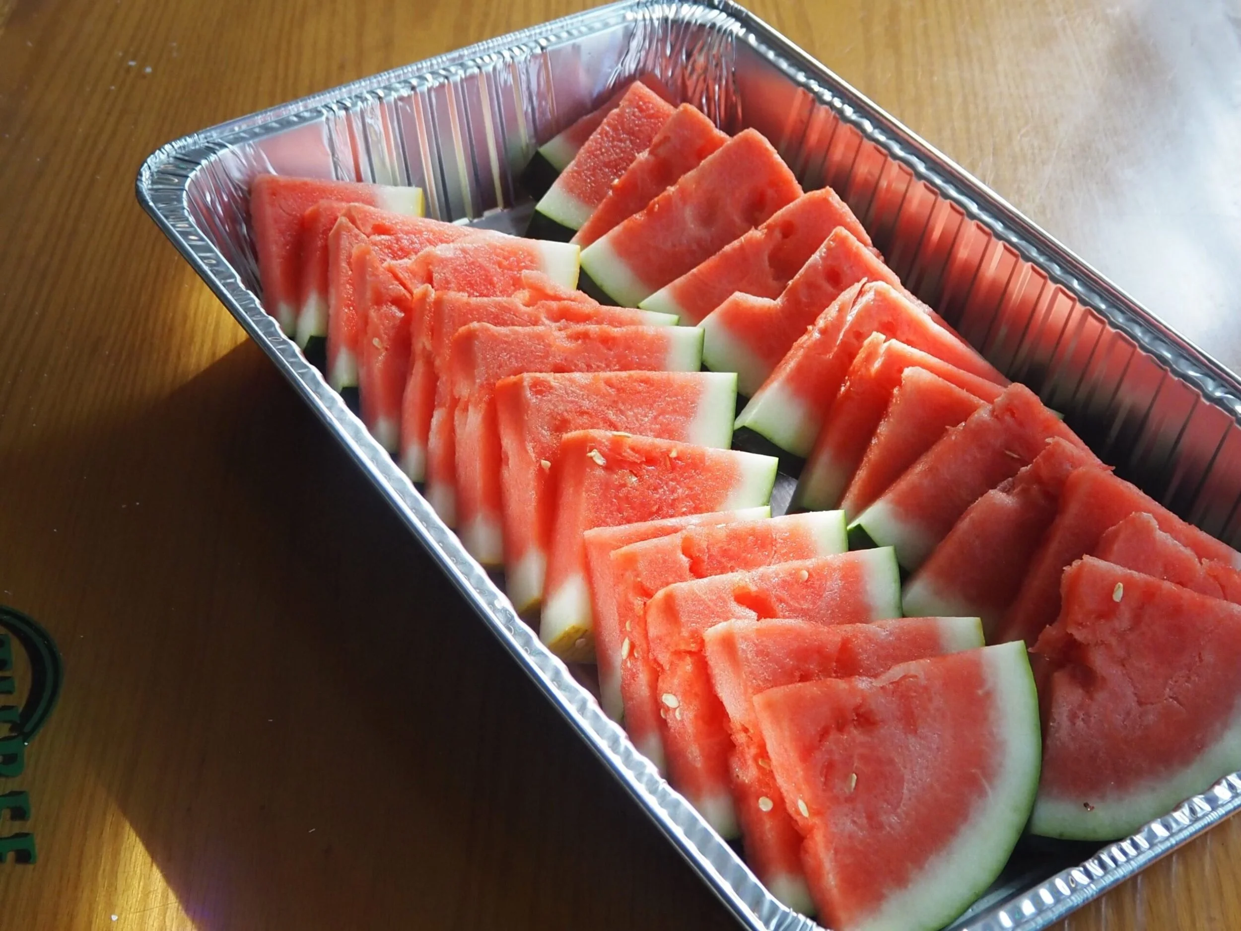 Tray of sliced watermelons arranged on a wooden table.