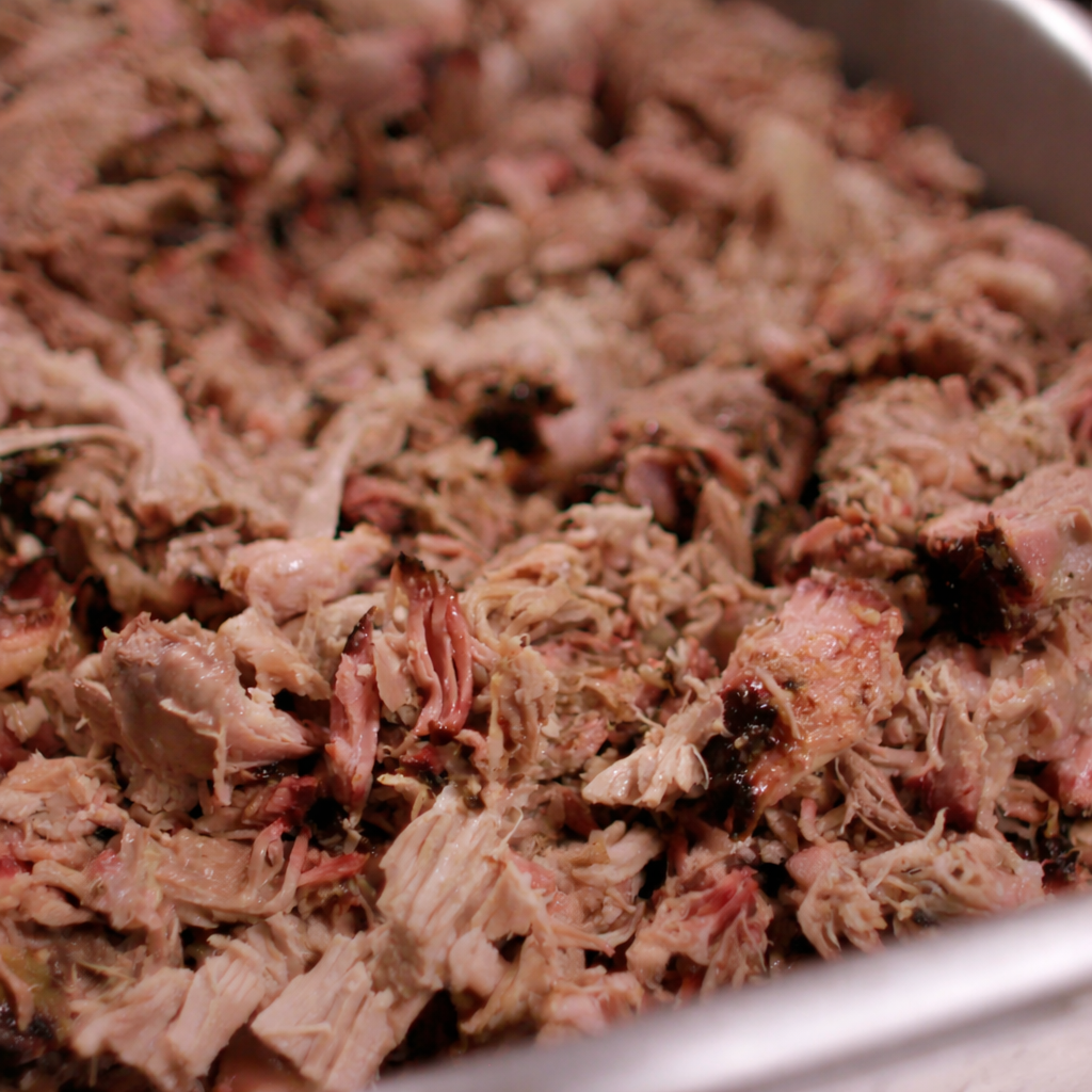 Cooked shredded meat in a metal container, likely pulled pork or chicken.