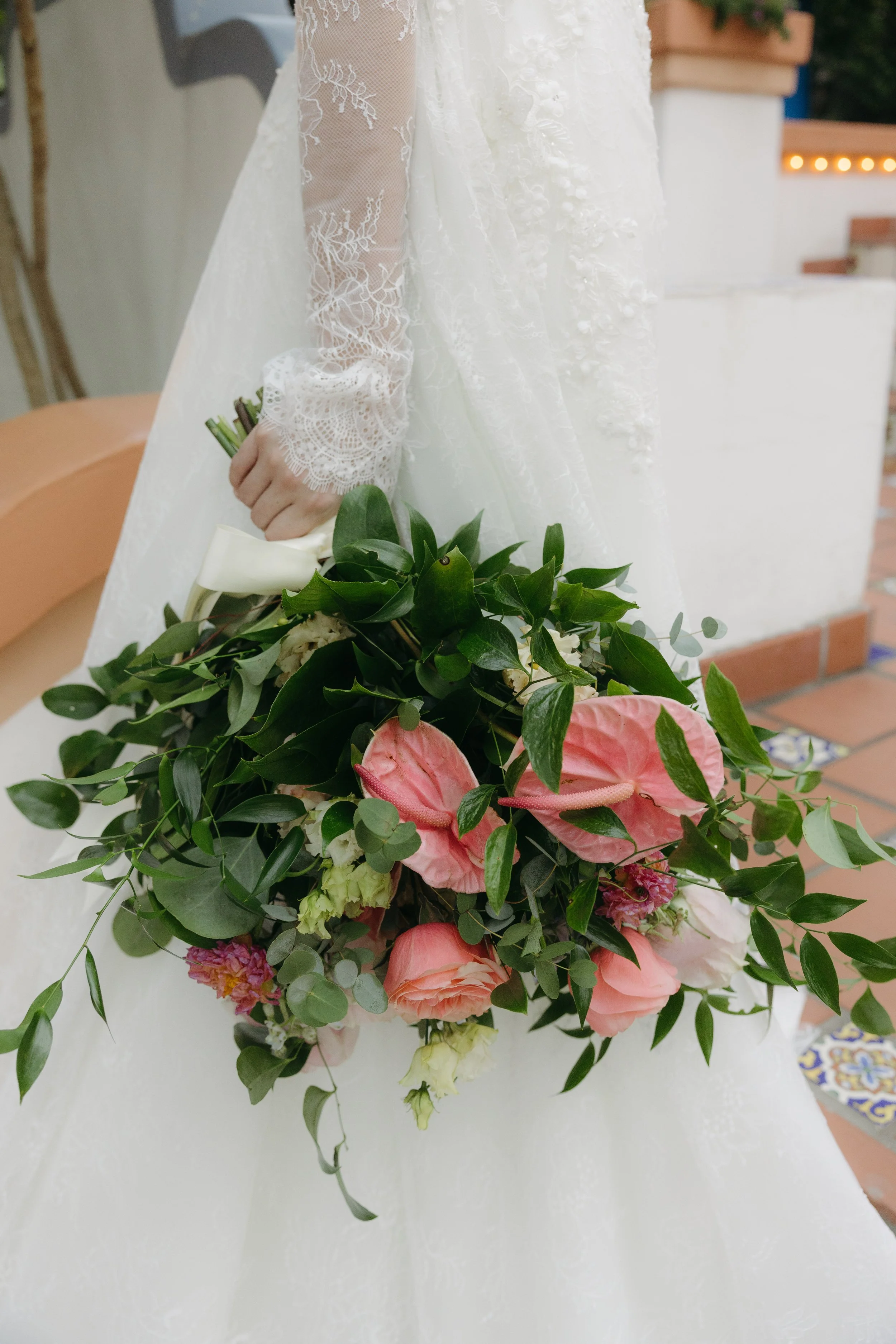 Bride dressed in a lace wedding gown holding a bouquet of pink and white flowers with greenery.