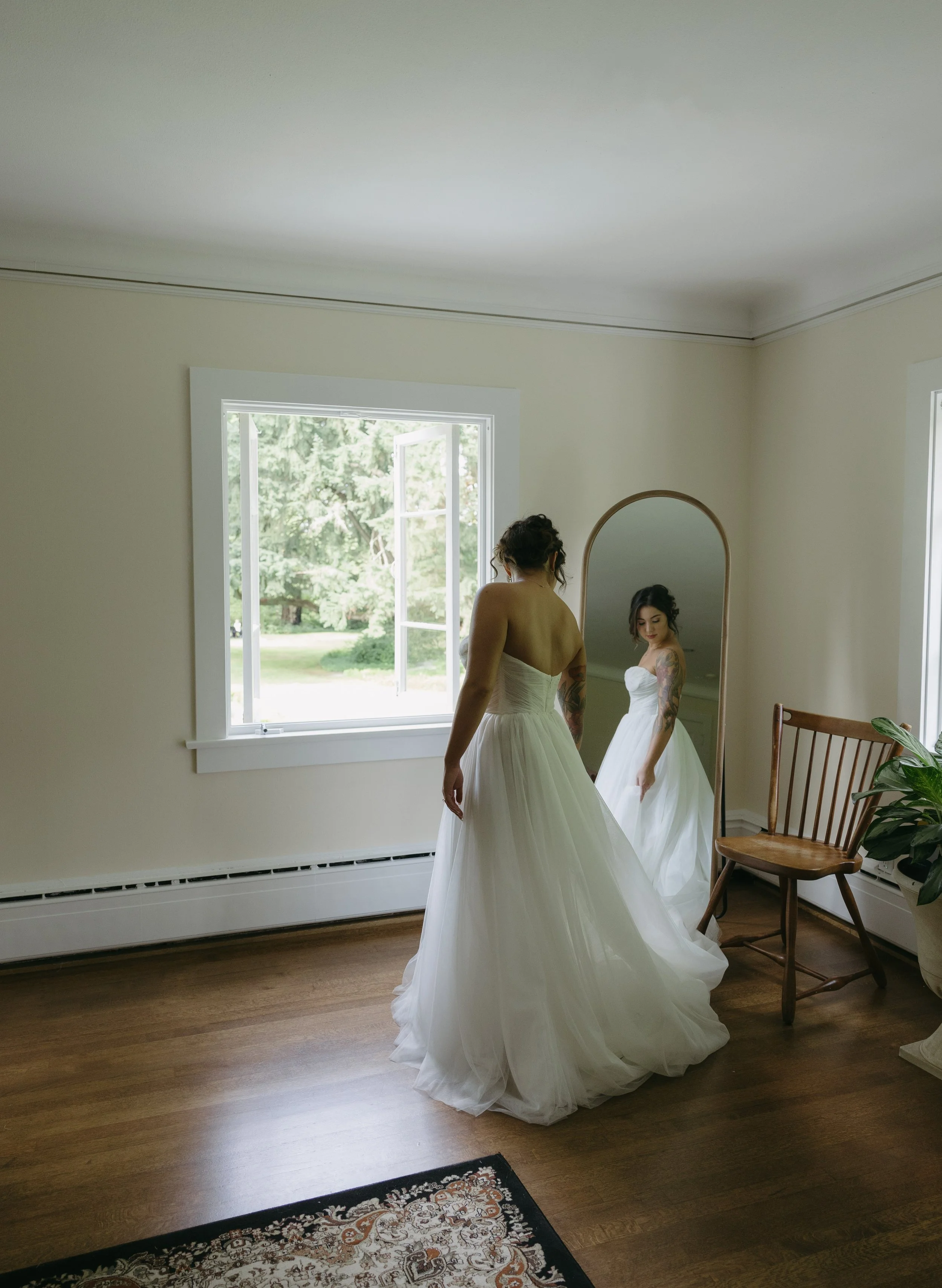 A bride in a white strapless wedding dress stands in a room, looking at her reflection in a tall mirror at a European inspired Lakewold Gardens wedding in Seattle