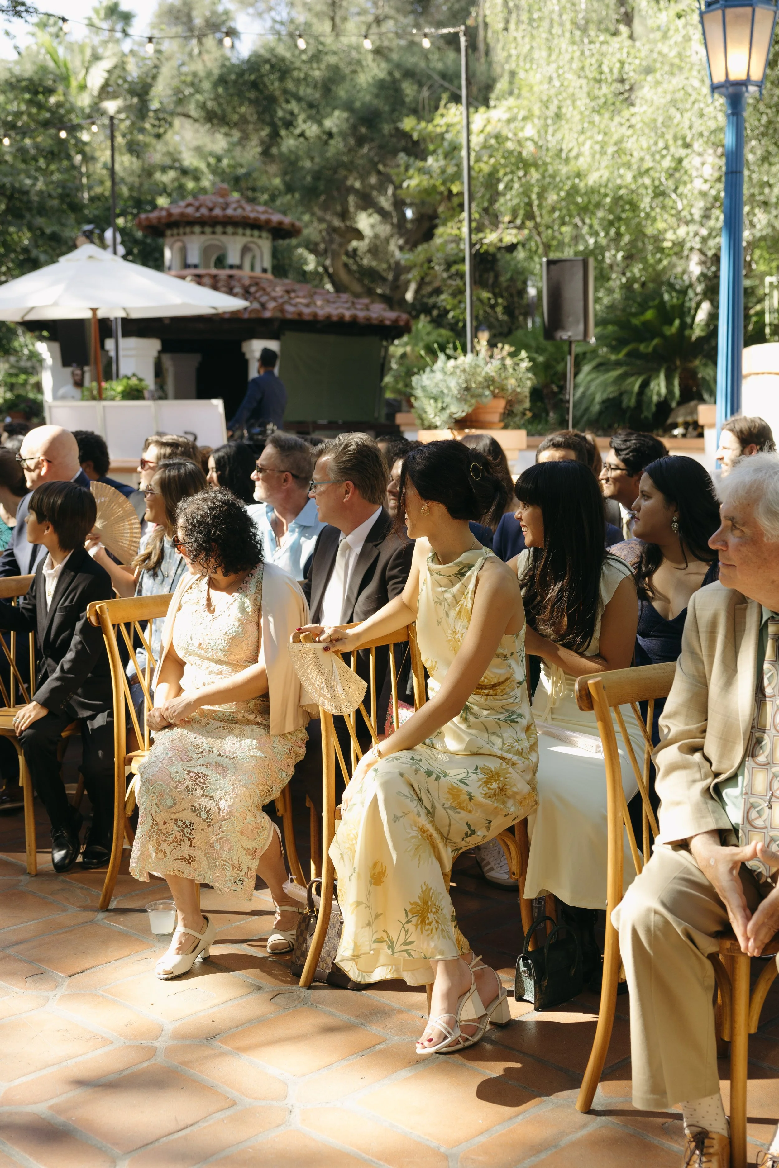 People seated outdoors at a wedding ceremony, under string lights with greenery and trees in the background at a Rancho Las Lomas Wedding in Los Angeles