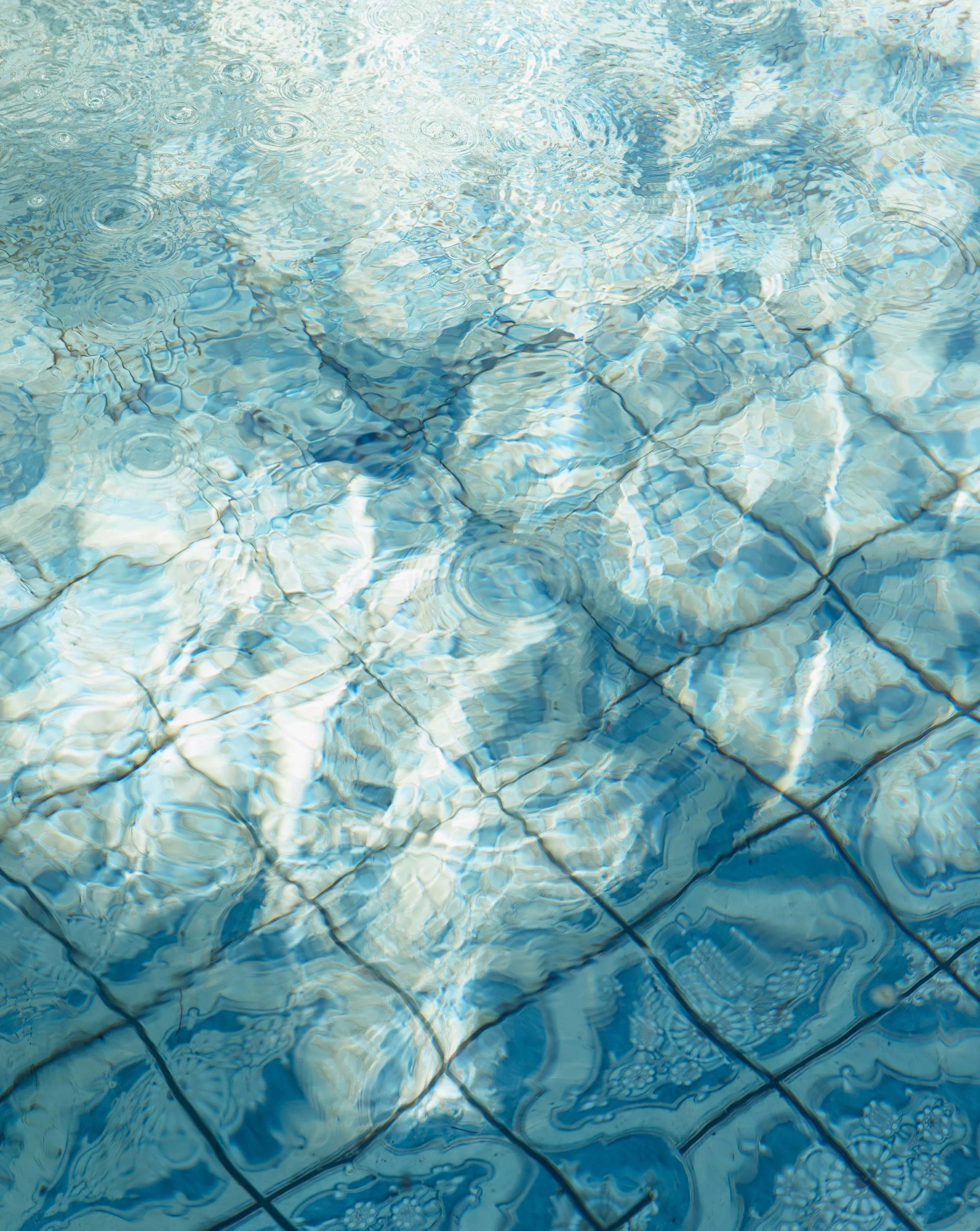 Close-up of a swimming pool's tiled floor under water with ripples and reflections.