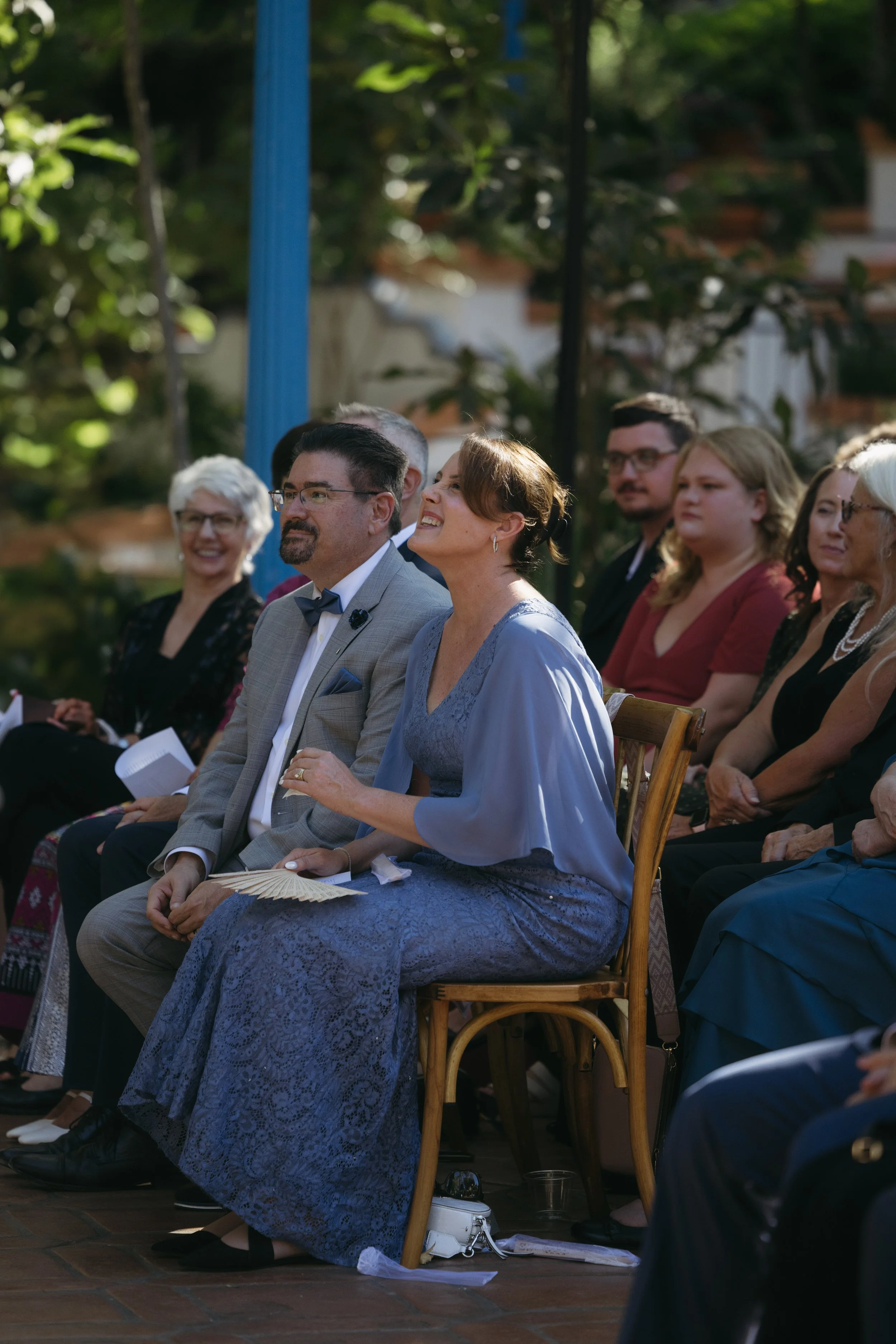 People sitting outdoors at a formal event, smiling and enjoying the moment.