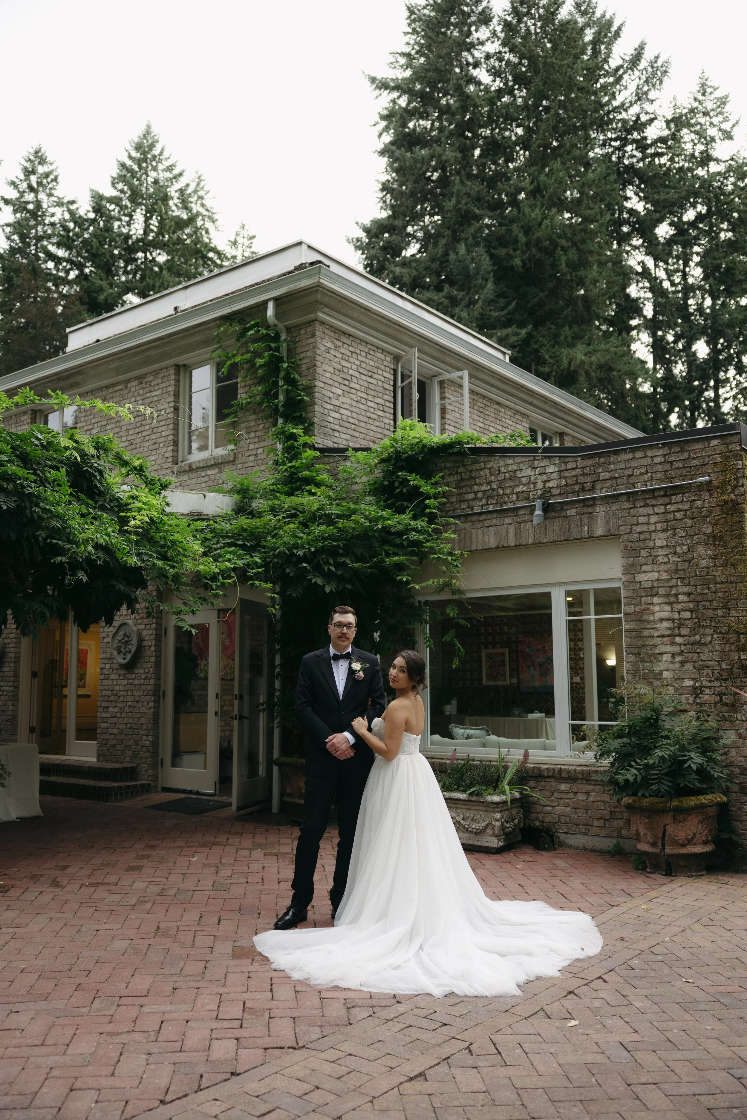 A bride and groom standing outside a brick building, with the bride in a white wedding gown and the groom in a black tuxedo at a European inspired Lakewold Gardens wedding in Seattle