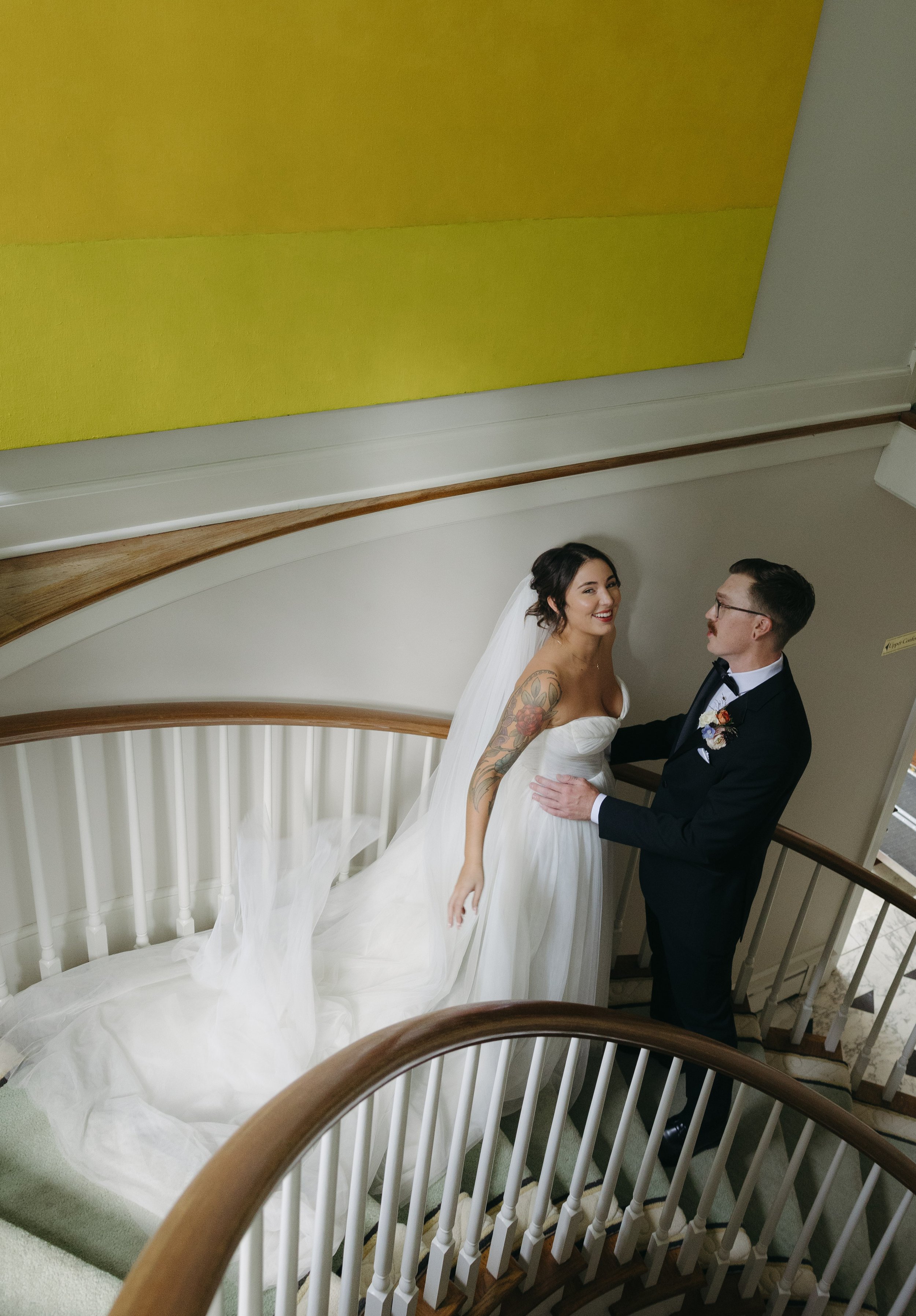 Bride and groom on a staircase, smiling at each other, holding hands, with the bride wearing a white wedding gown and veil, and the groom wearing a dark suit with a bow tie at a European inspired Lakewold Gardens wedding in Seattle