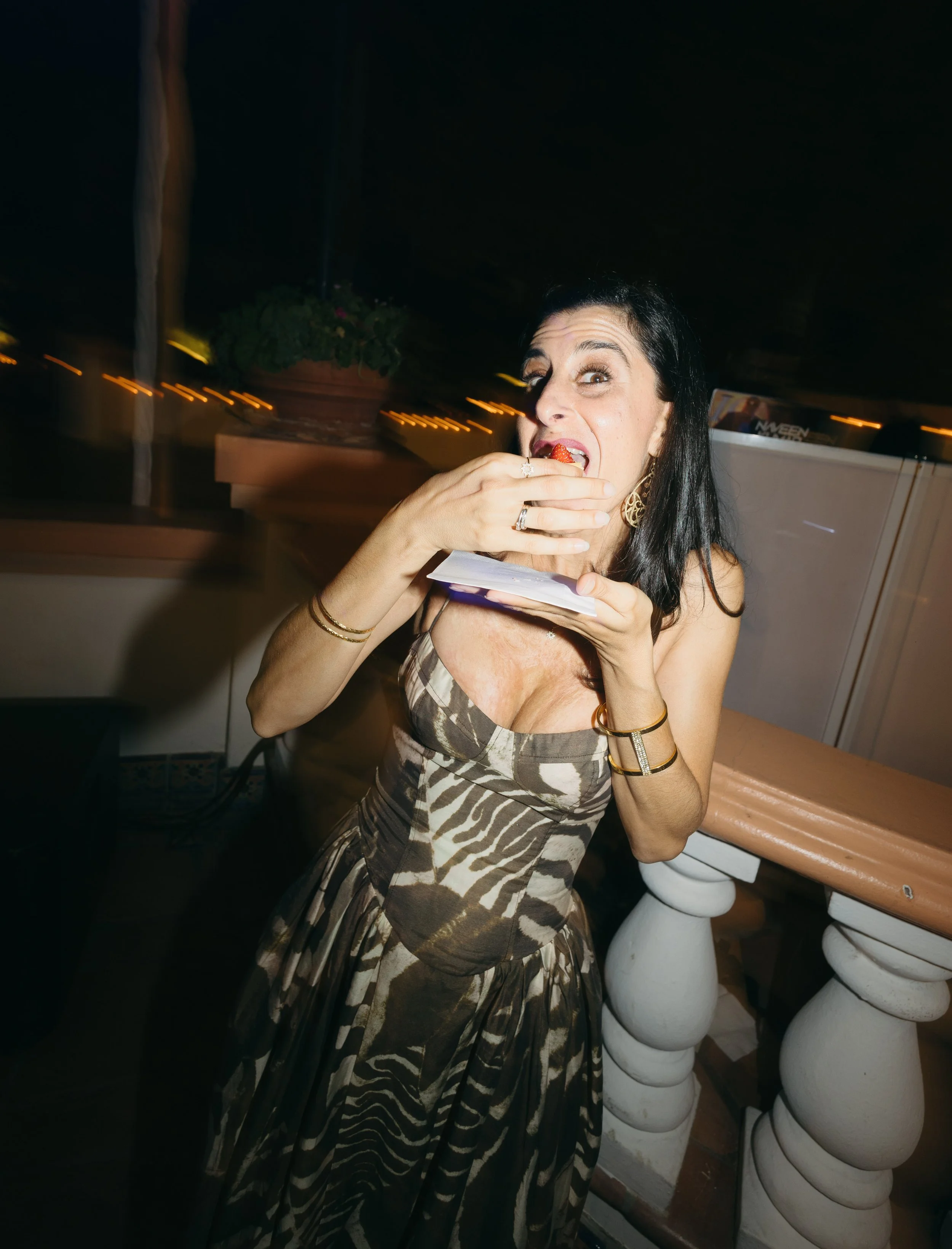 Woman in animal print dress eating a strawberry at a restaurant or bar at night.