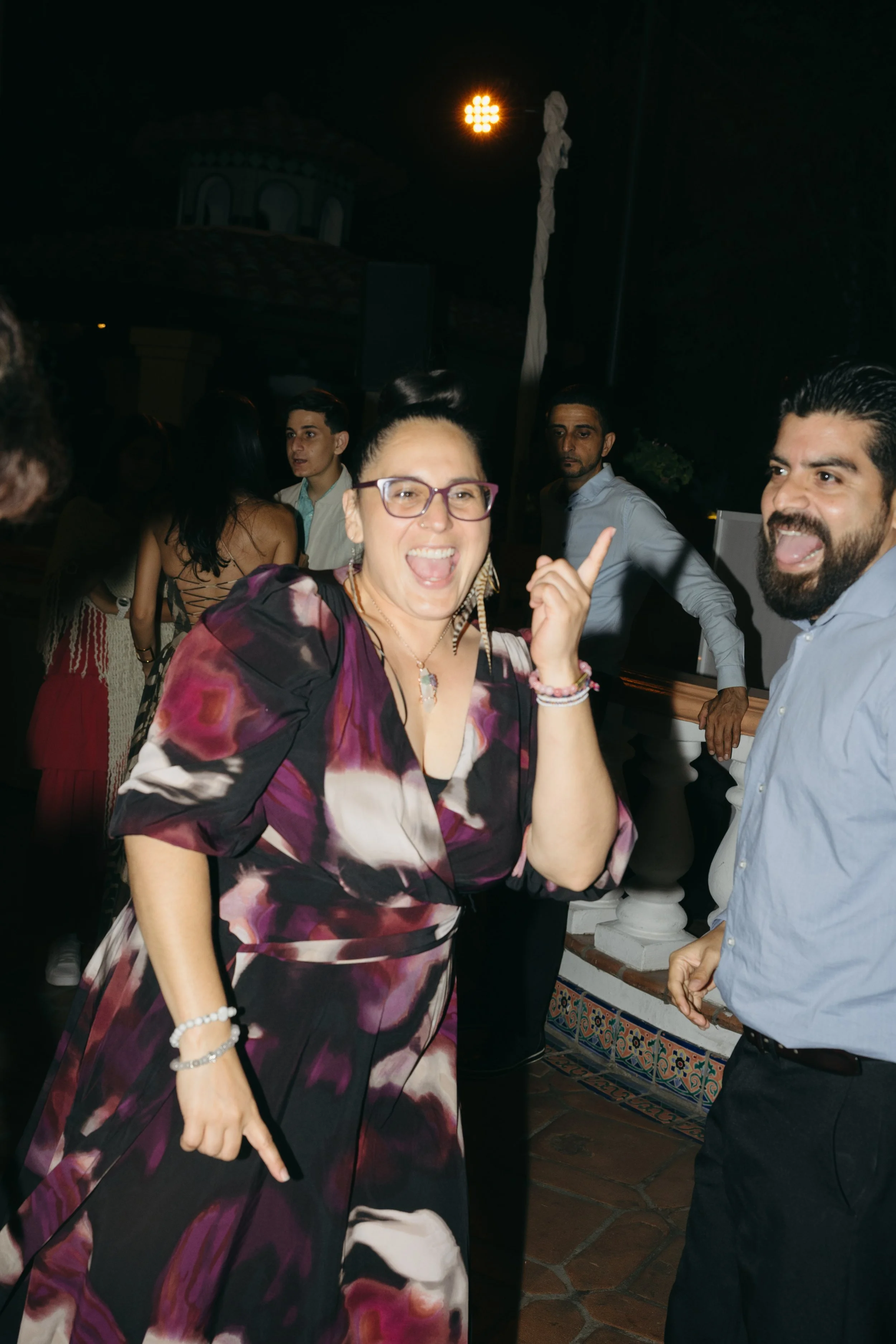 People dancing and enjoying at a party, with a woman pointing and smiling at the camera.