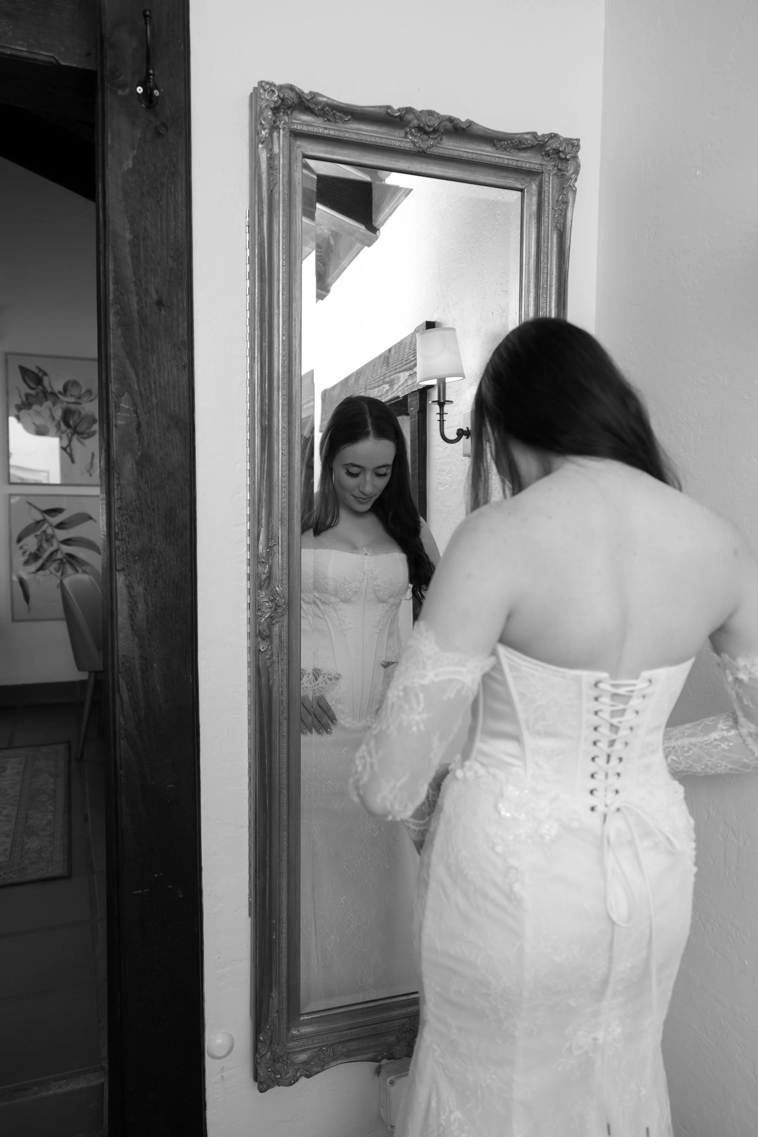 A woman in a wedding dress looking at herself in a full-length mirror.