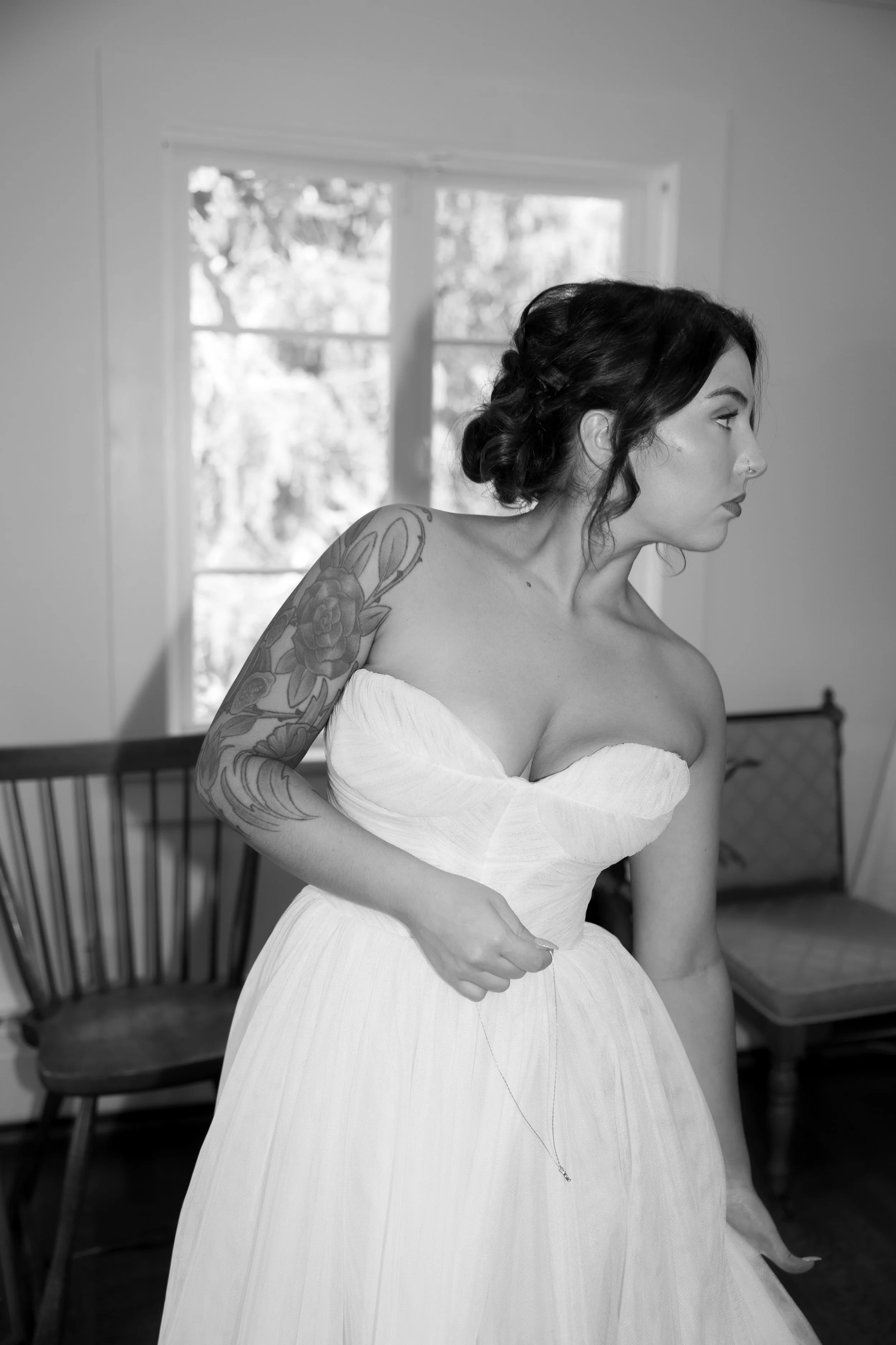 A woman in a strapless wedding dress standing indoors, with a window behind her.
