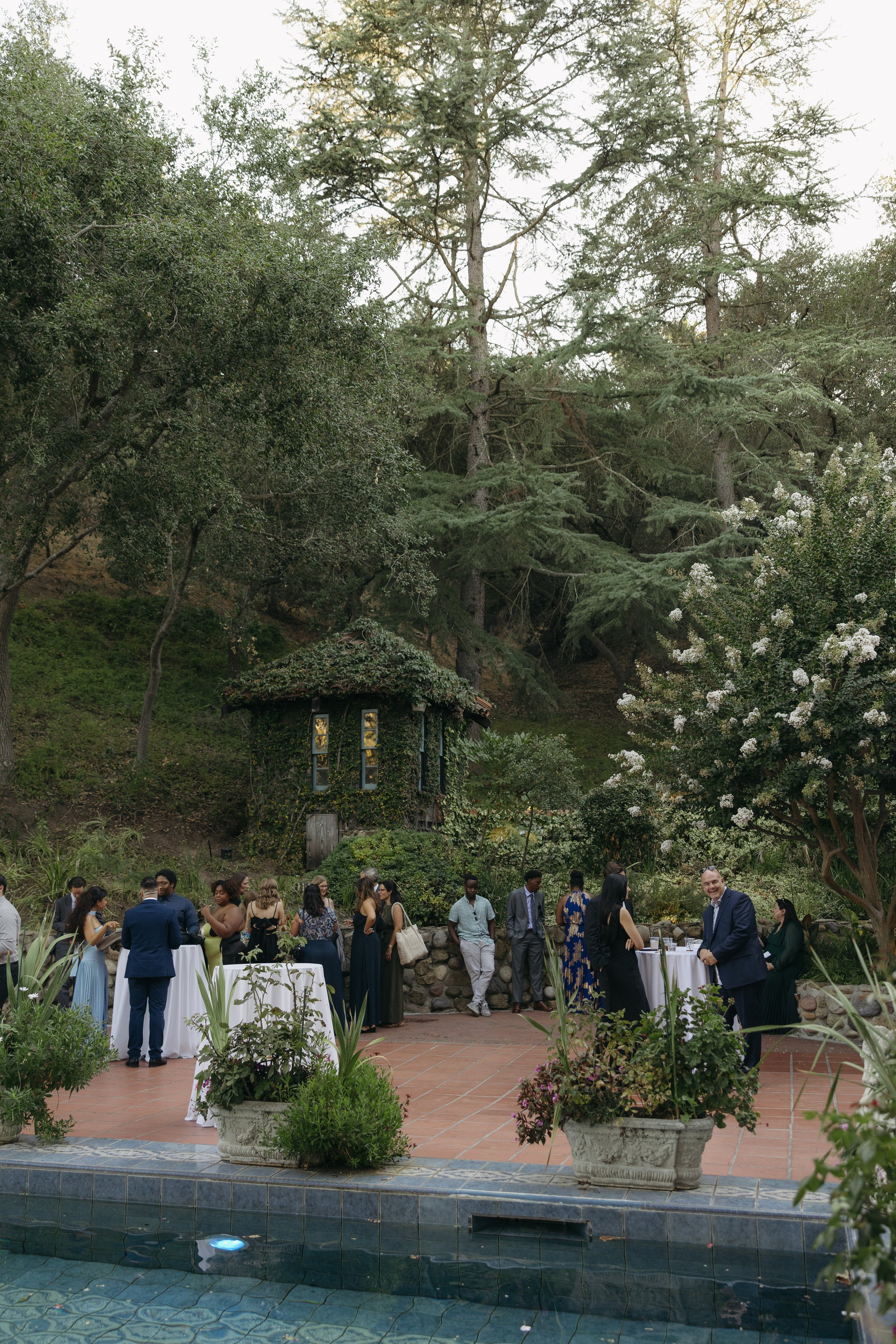 People gathered at a social event outdoors near a pool, with trees and greenery in the background at cocktail hour at a Rancho Las Lomas Wedding in Los Angeles