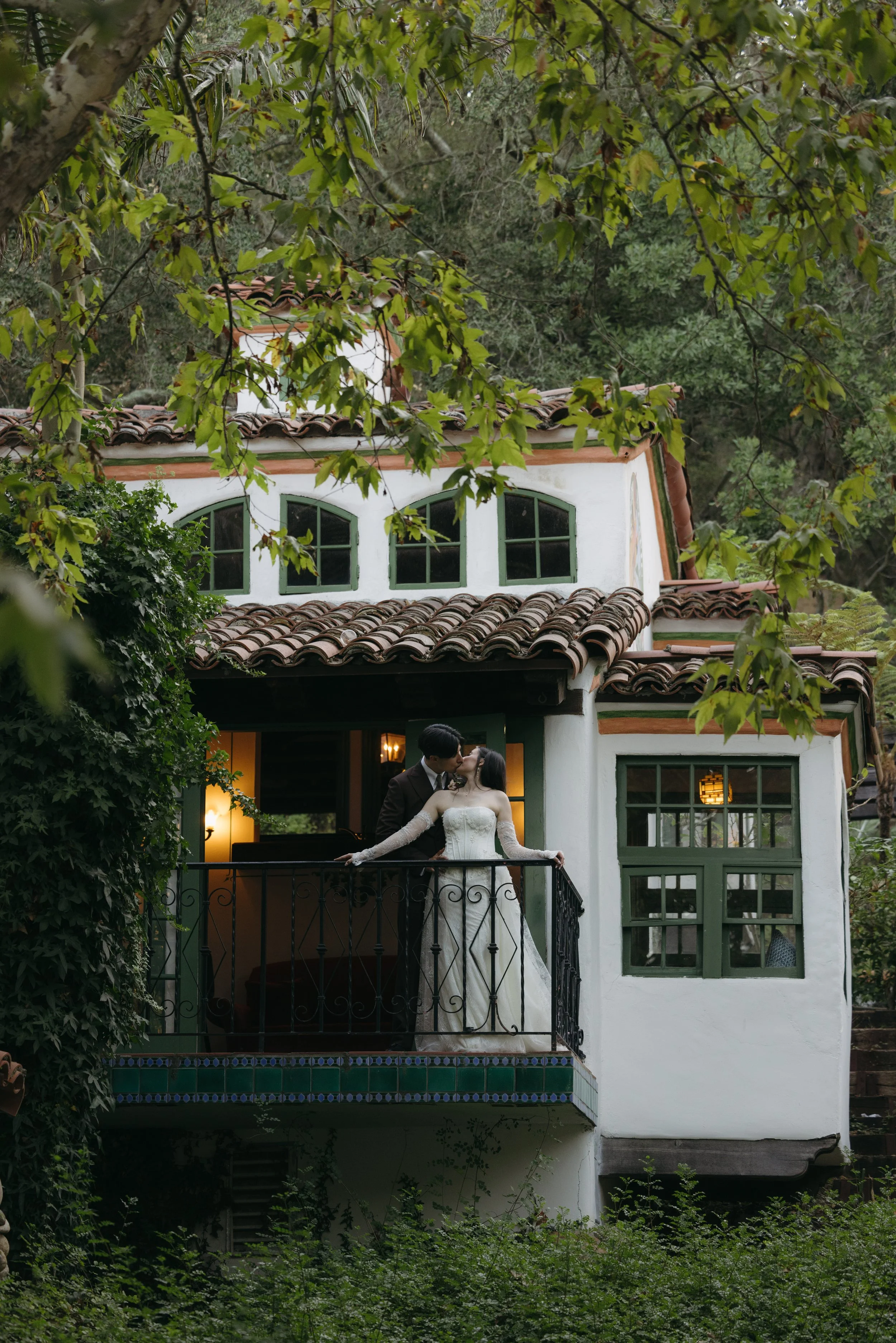 A bride and groom sharing a kiss on the balcony of a rustic house surrounded by greenery at a Rancho Las Lomas Wedding in Los Angeles