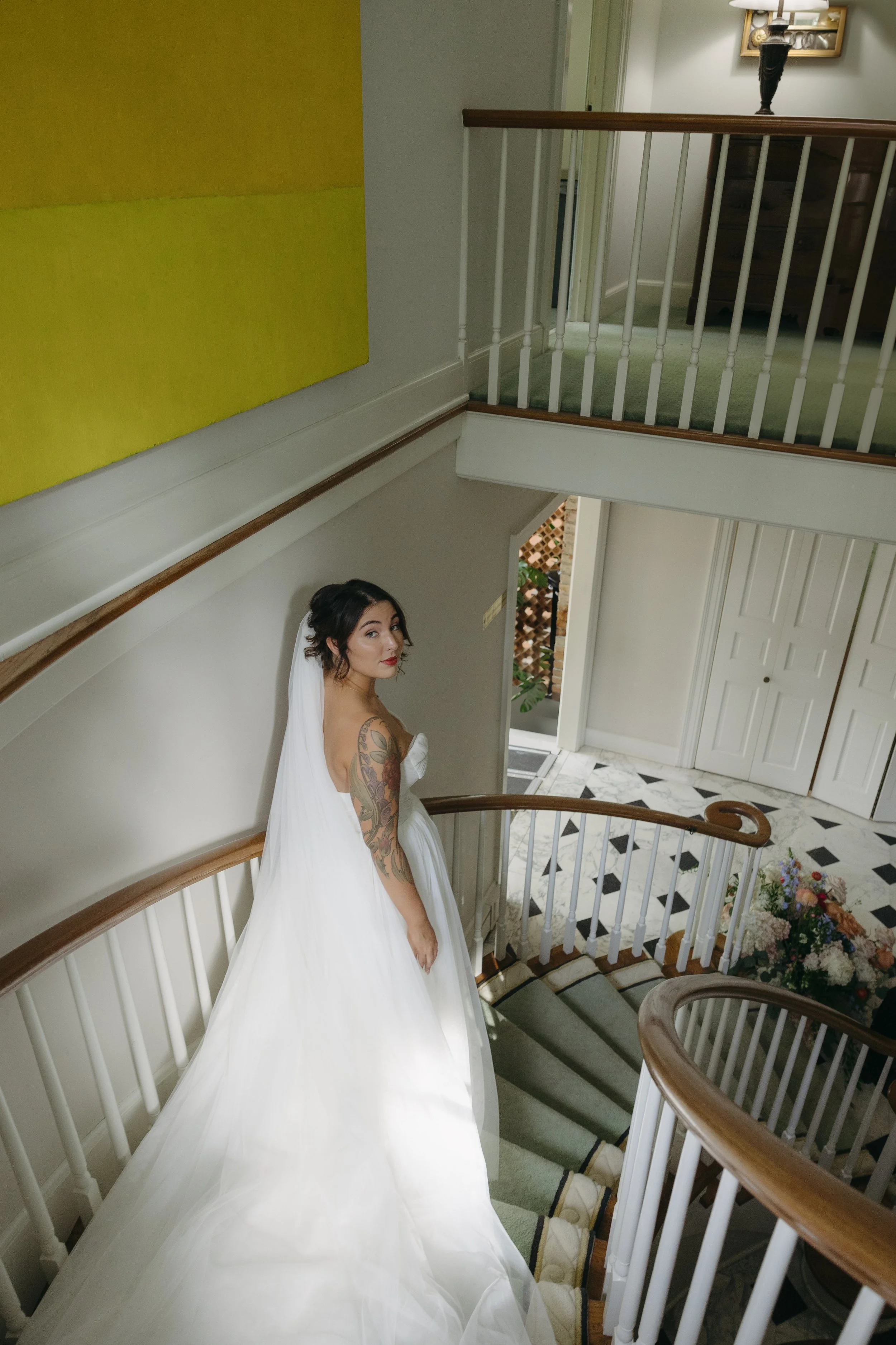 A bride in a white wedding dress with a train, standing on a staircase, looking over her shoulder at the camera during her first look at a European inspired Lakewold Gardens wedding in Seattle
