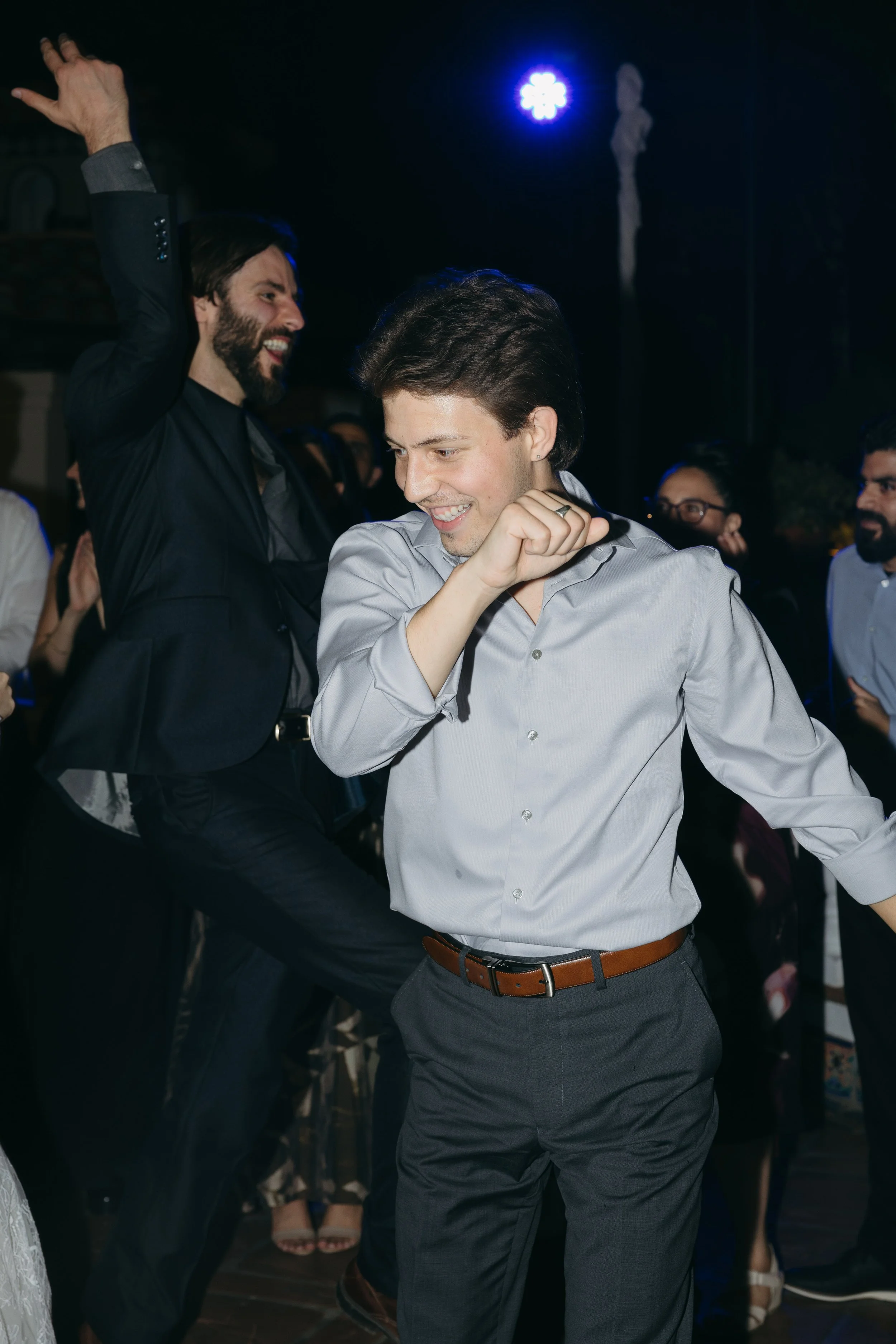 People dancing at a party, with two men in the foreground smiling and enjoying the music.