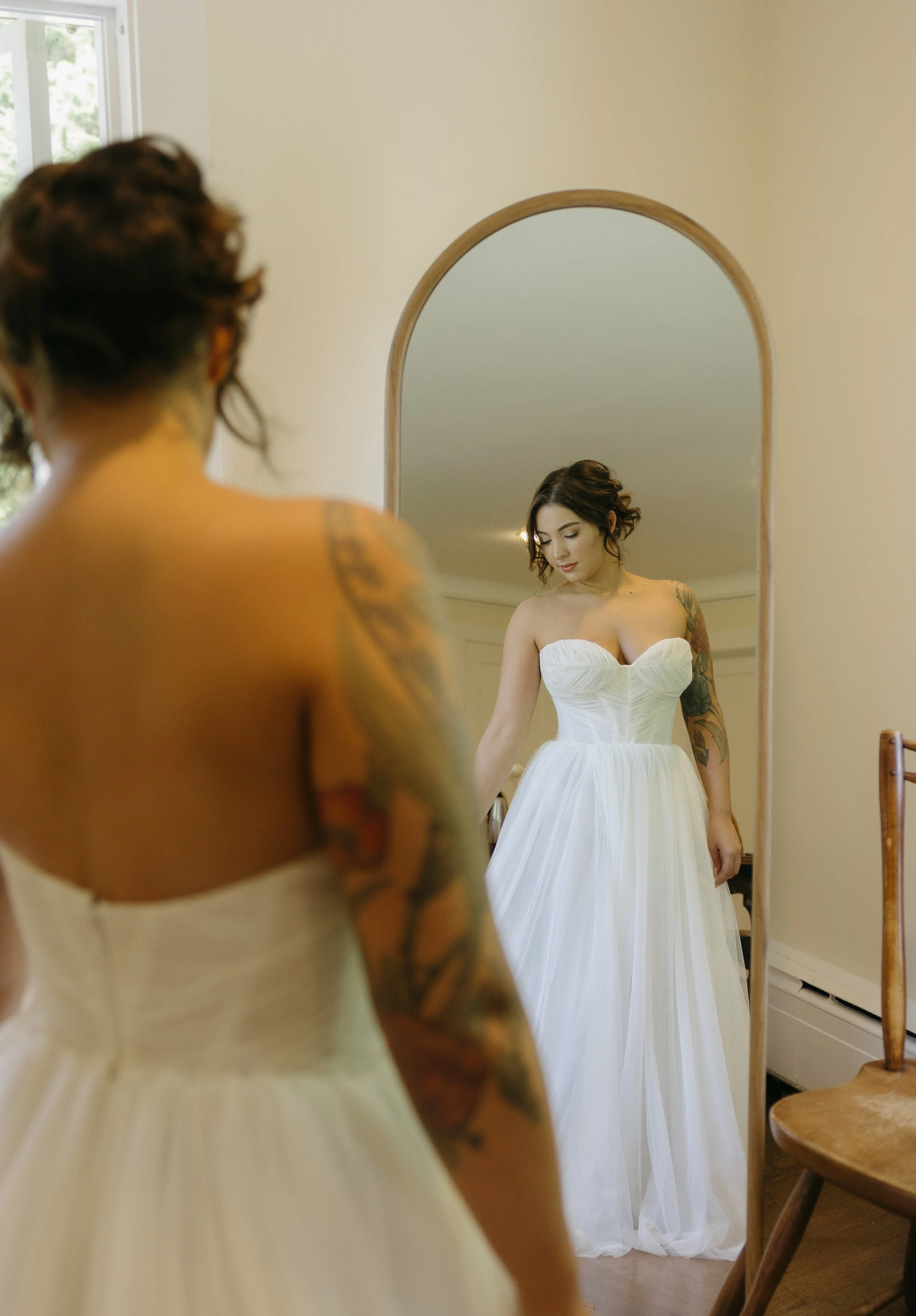 A bride in a white wedding dress looking at herself in a full-length mirror at a European inspired Lakewold Gardens wedding in Seattle
