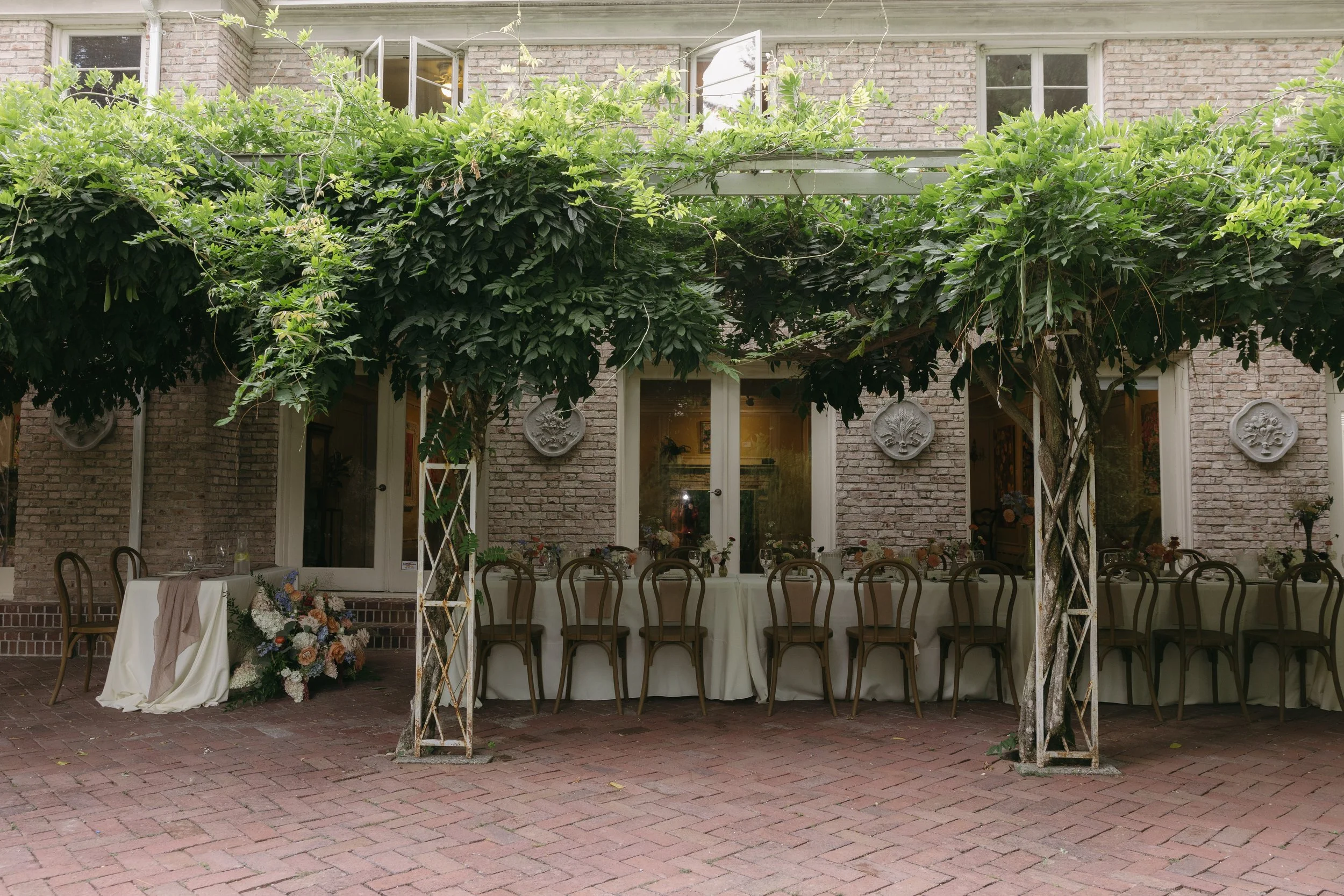Outdoor reception area set up with long table and chairs under a leafy pergola, at a European inspired Lakewold Gardens wedding in Seattle