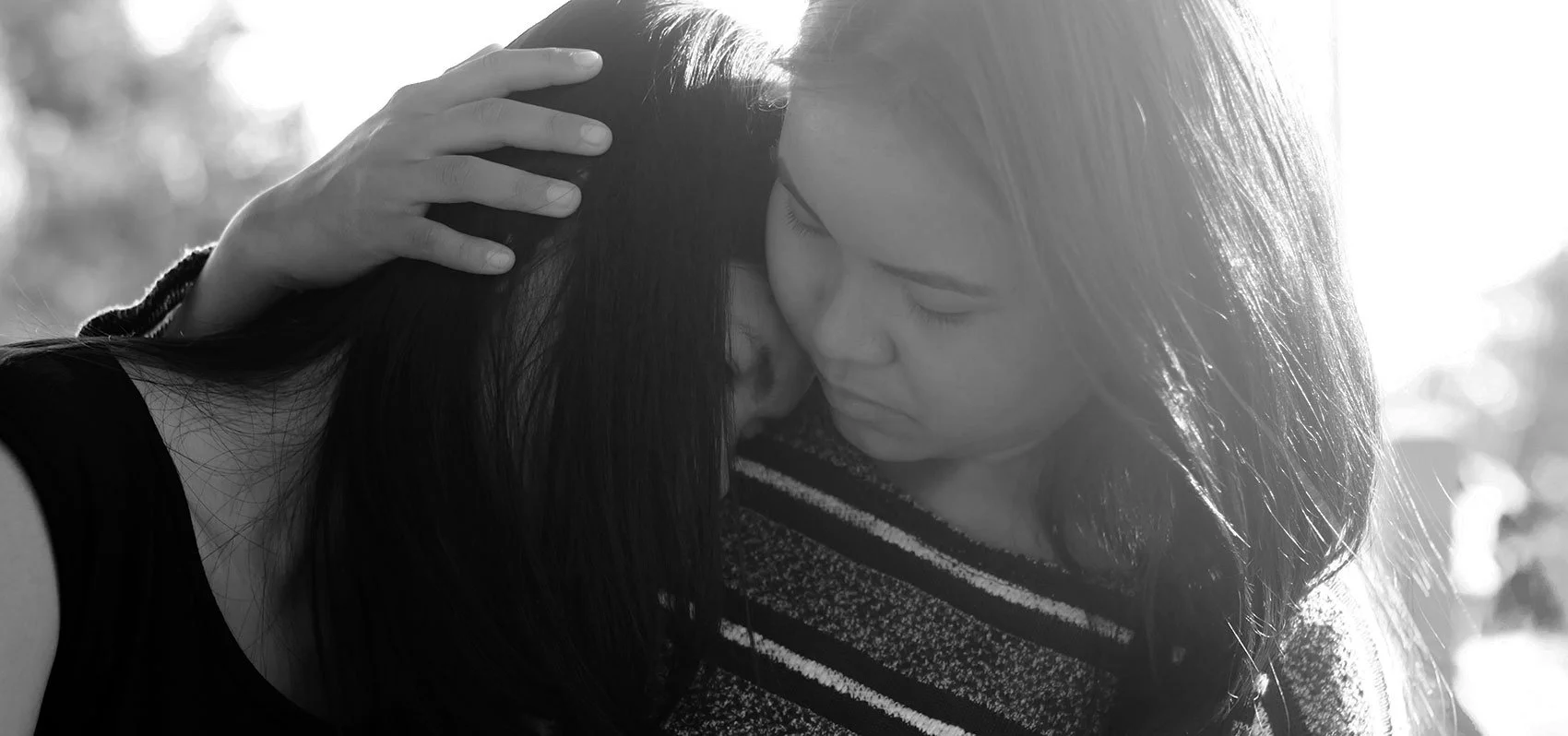 Two women share a close, tender moment with one woman gently holding the other’s head as she leans in, both with eyes closed.