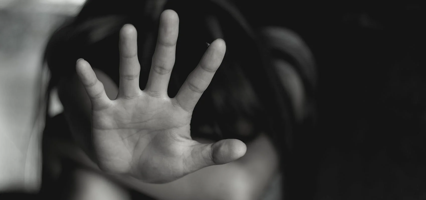 A child's open hand reaching out with fingers spread, black and white photograph, blurred background.