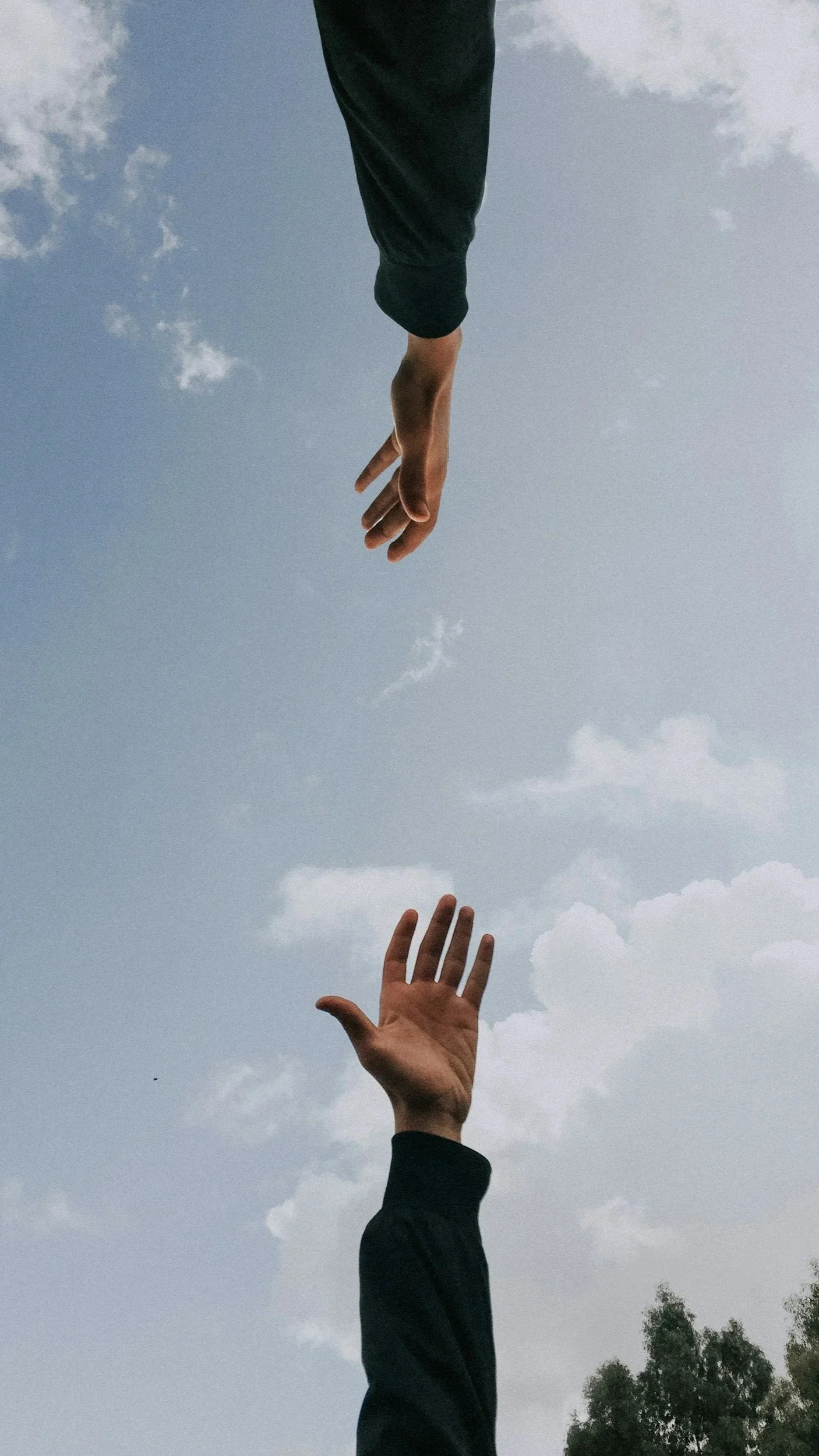Two hands reaching towards each other against a cloudy sky, one hand is above and the other is below.