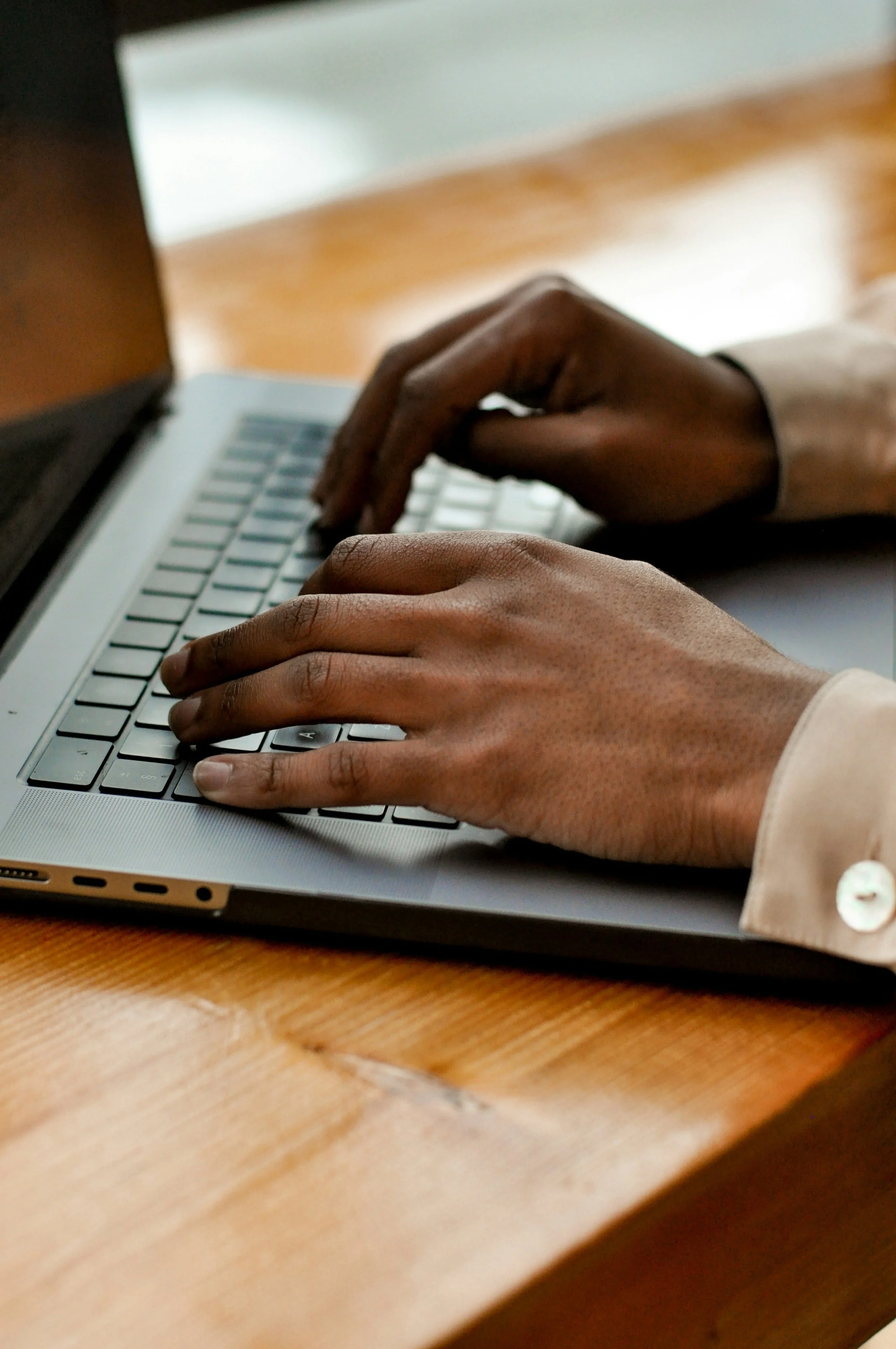 Close-up of hands typing on a laptop keyboard on a wooden desk.
