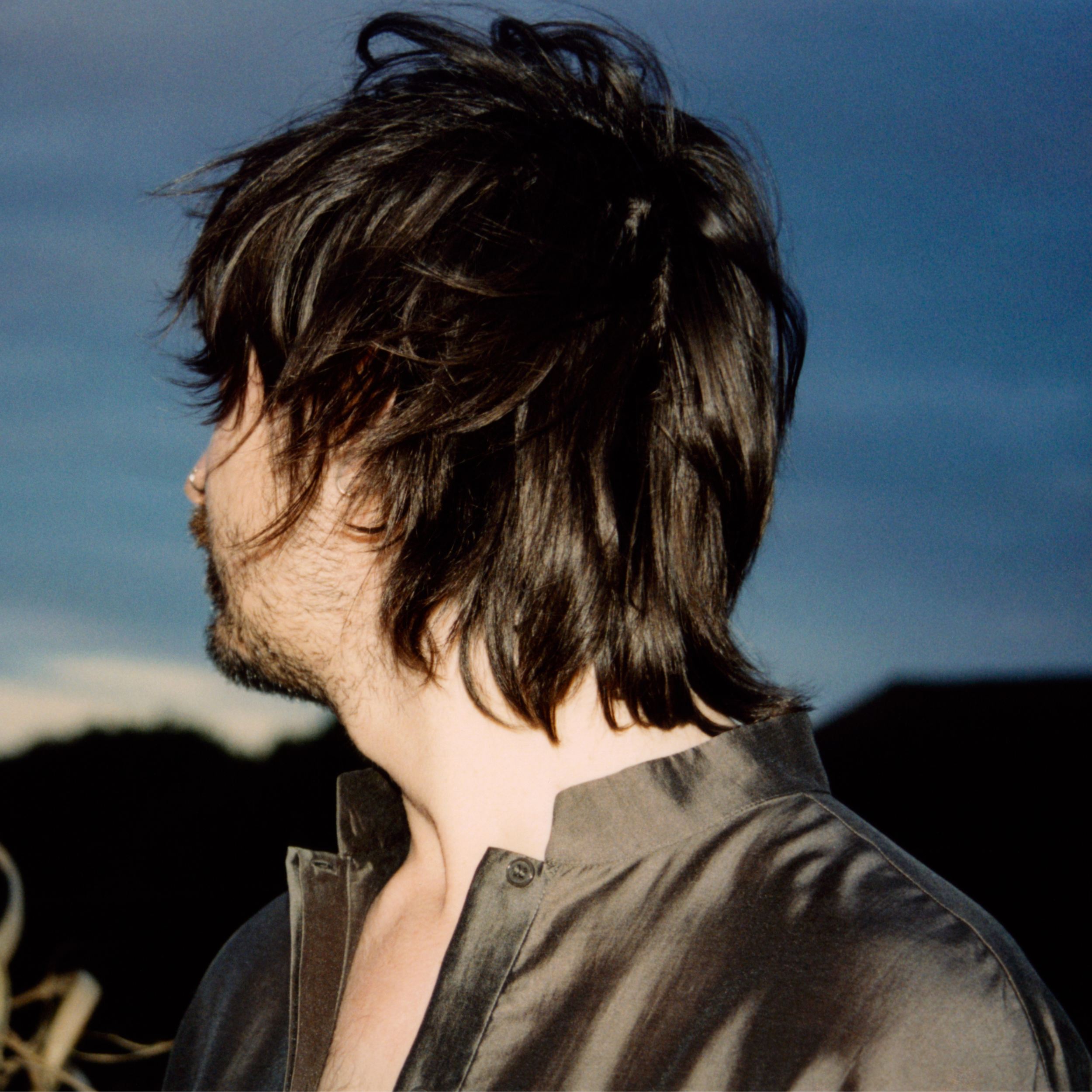Close-up of a person's messy brown hair and part of their face against a clear blue sky.