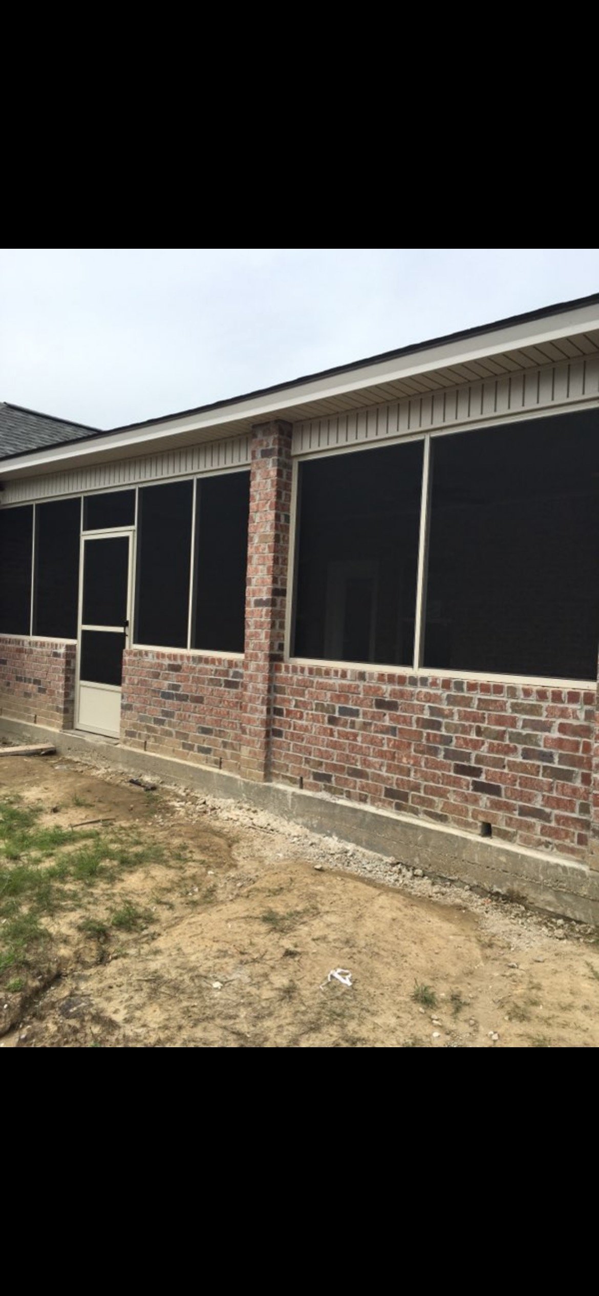 The image shows a brick house with a screened-in porch, a dirt yard in the foreground, and an overcast sky above.