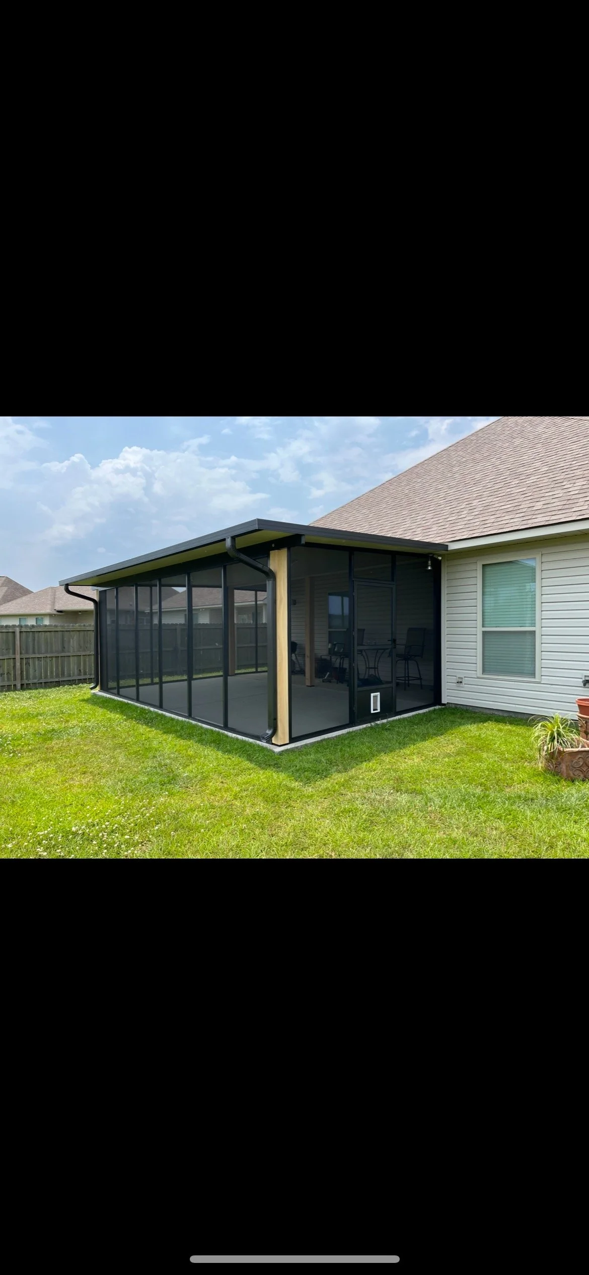 A screened-in porch attached to a house, with outdoor seating and a grassy backyard, under a partly cloudy sky.