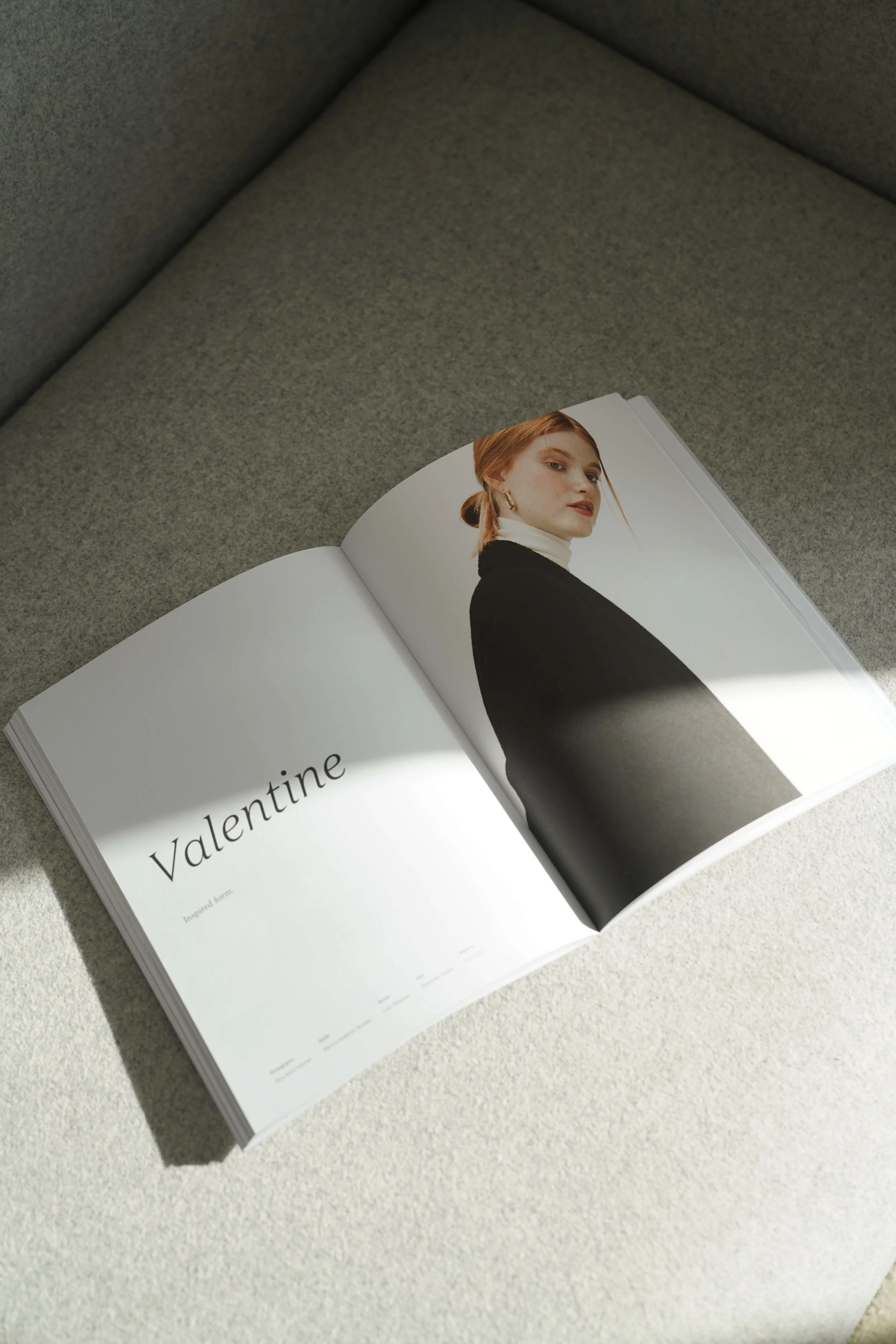 Open magazine on a light-colored surface, featuring a portrait of a woman with red hair, wearing a black top and earrings, with the text "Valentine" on the opposite page.