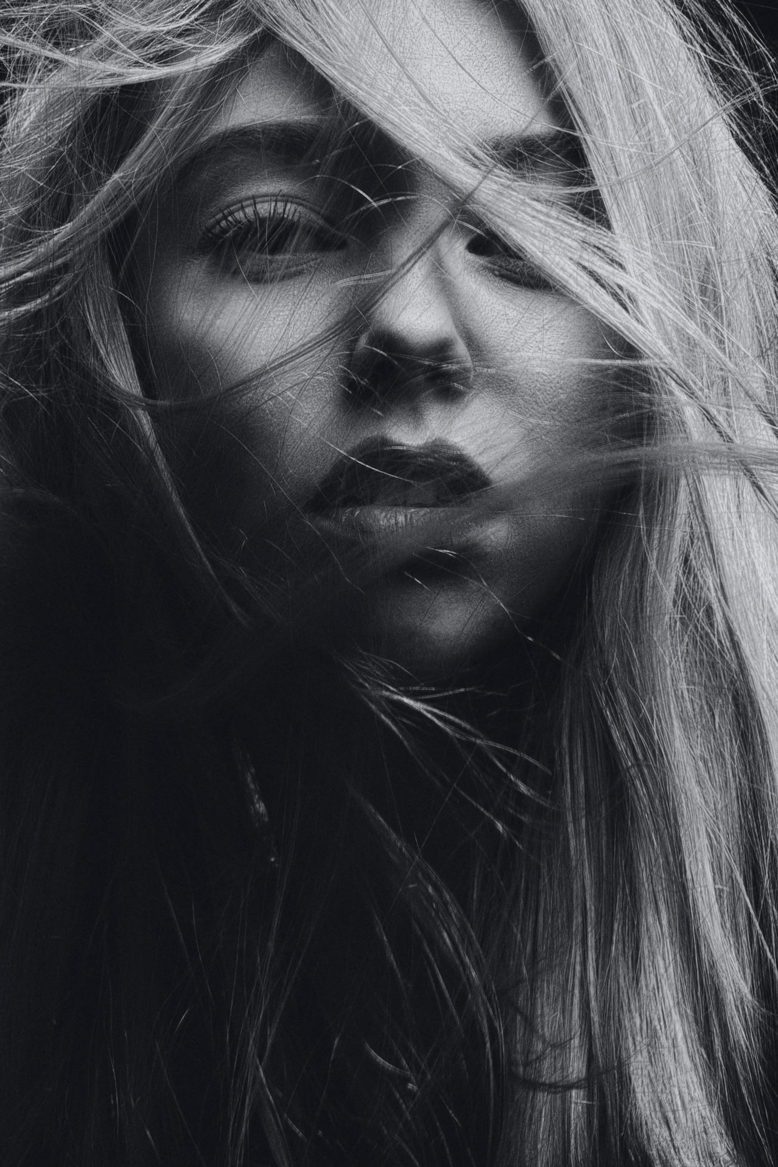 Close-up black-and-white portrait of a woman with long, tousled hair partially covering her face.