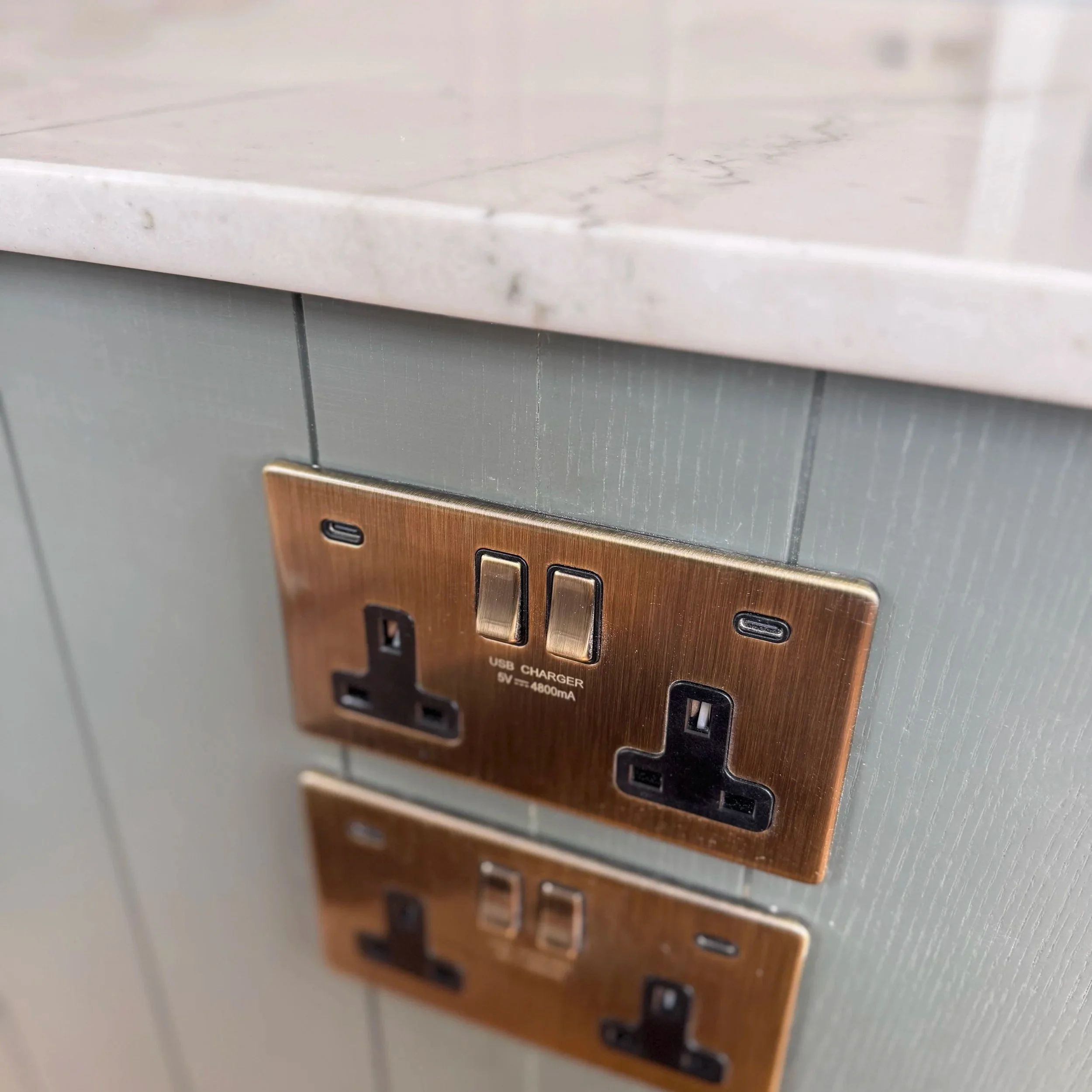 Close-up of electrical outlets and USB chargers embedded in a wall near a light-colored stone countertop.