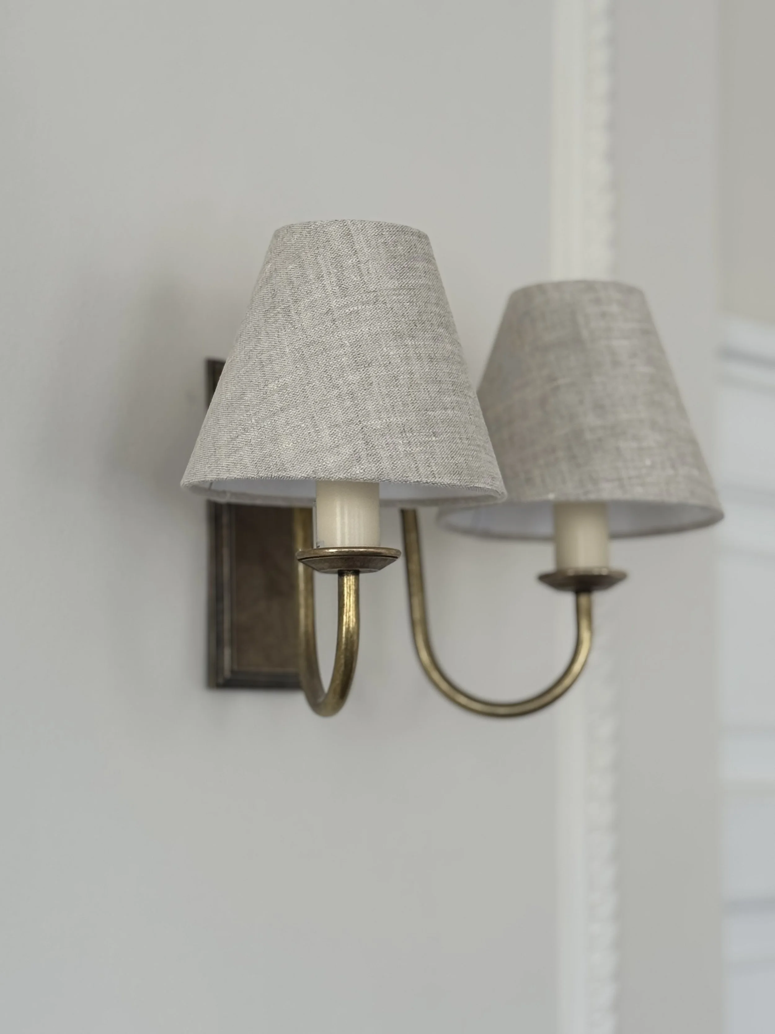 Wall-mounted double arm wall sconce with beige fabric lampshades and brass finish