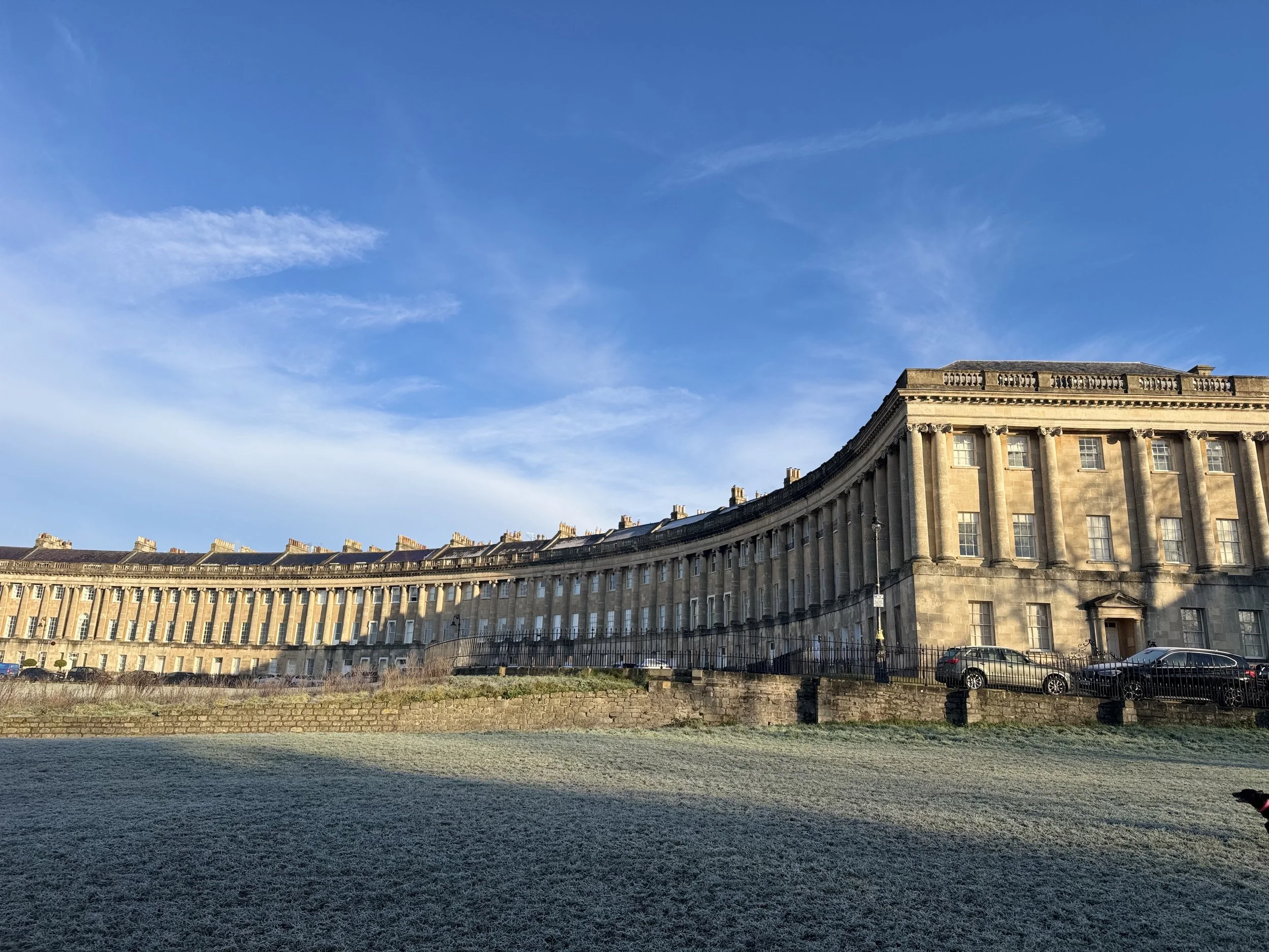 The Royal Cresent in the city of Bath. A curved historic Georgian building with columns on a sunny day under a blue sky.