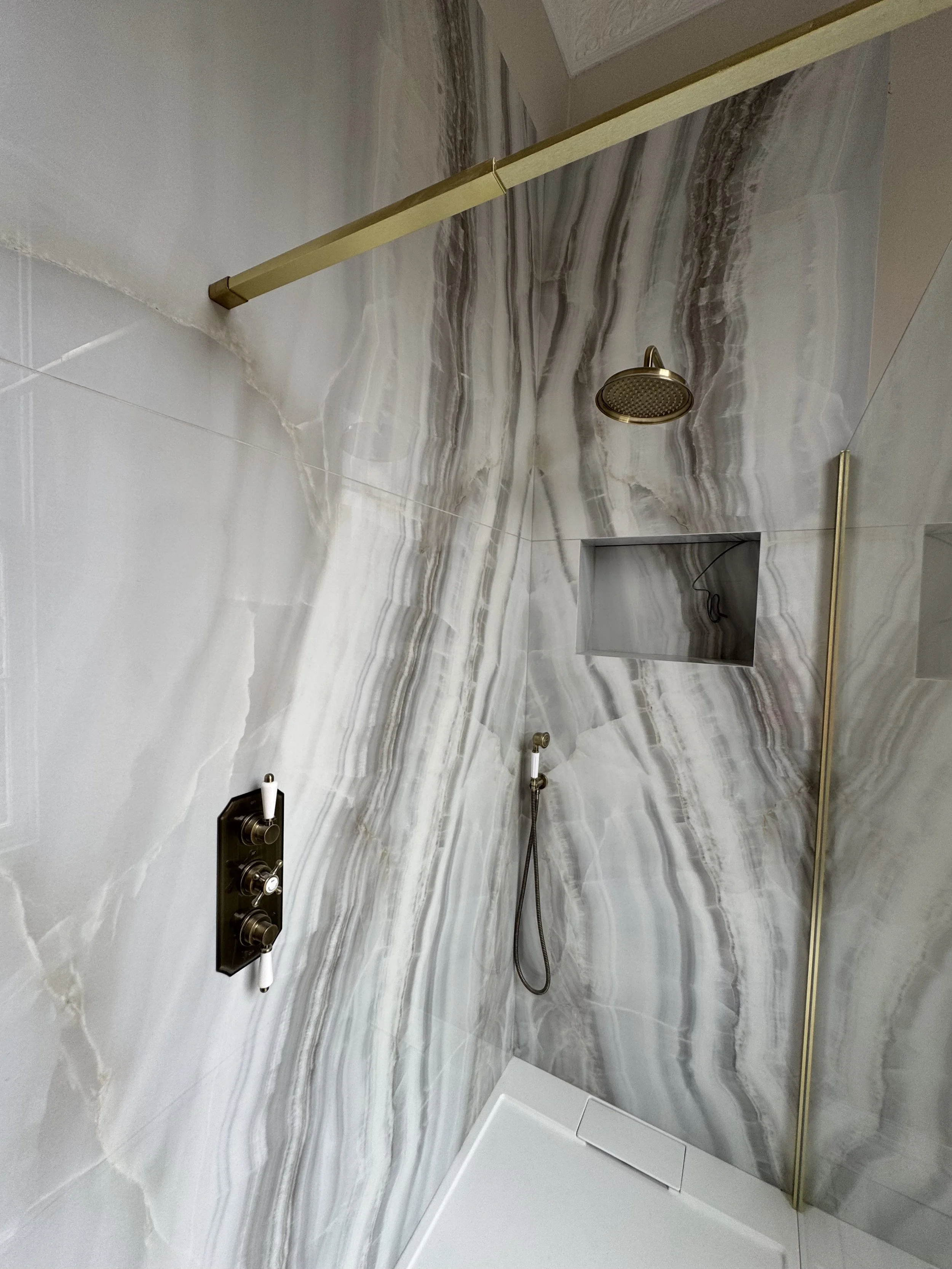 Modern marble shower with gold accents, wall niche, and rainfall showerhead.