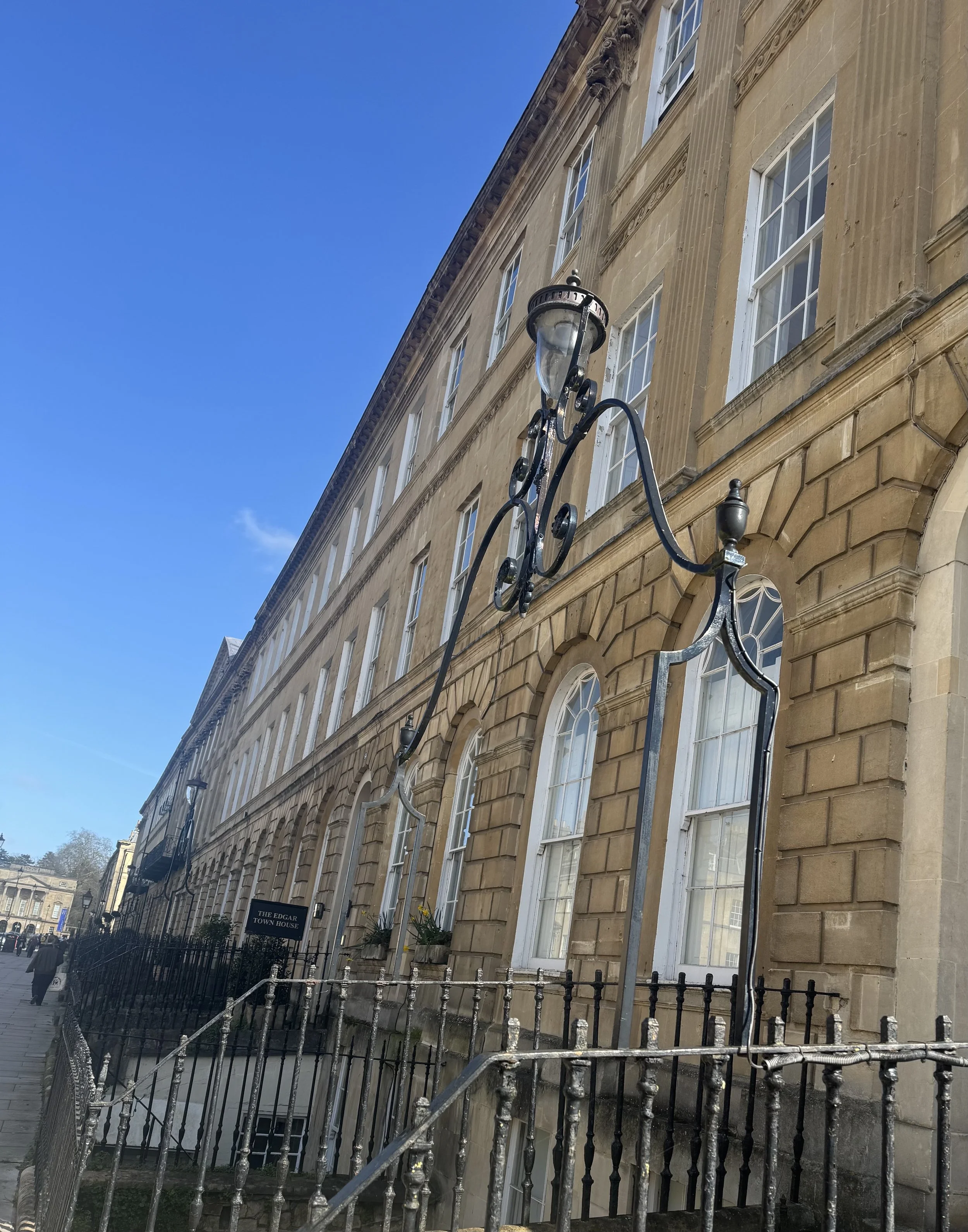 A Georgian townhouse with tall sash windows with an ornate street lamp mounted on the building's exterior, under a clear blue sky.