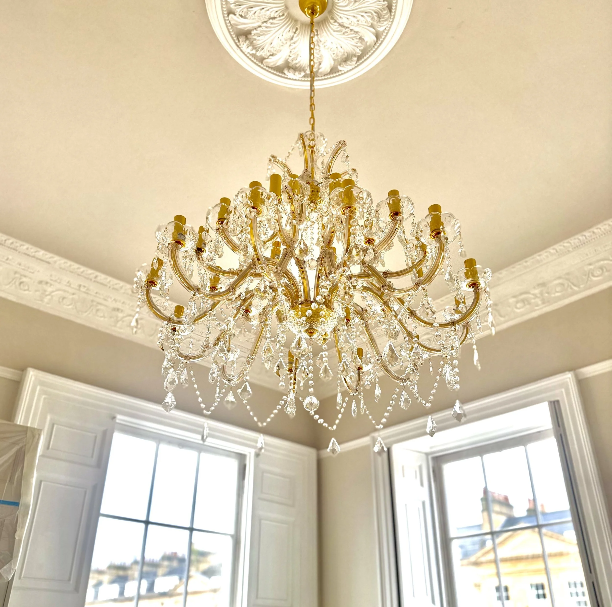 Elegant chandelier with crystal decorations hanging from a decorative ceiling medallion in a room with large windows.