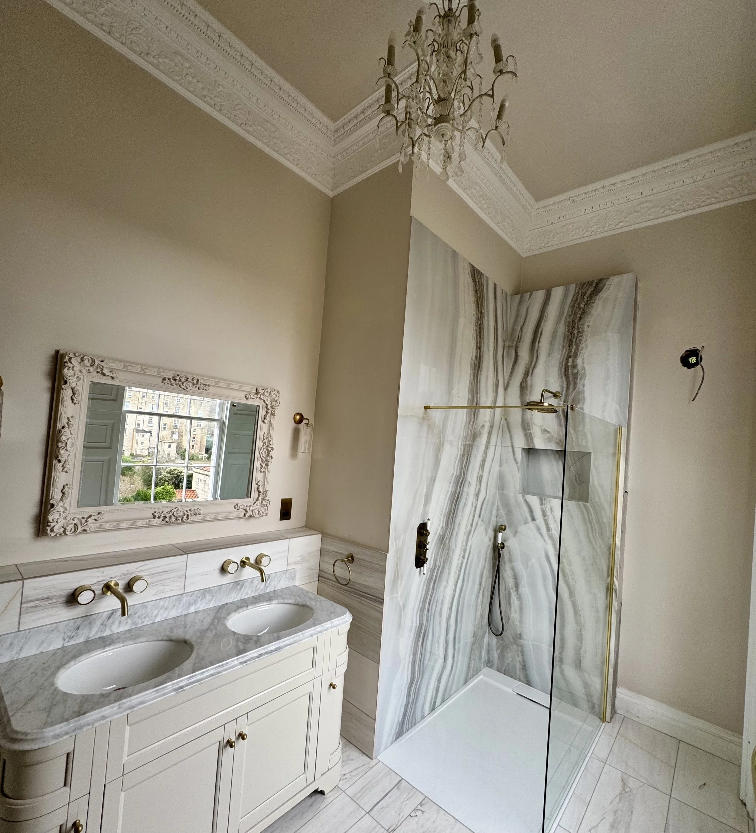 Luxurious bathroom with dual sinks, ornate mirror, and a marble shower with glass door and antique brass fixtures.