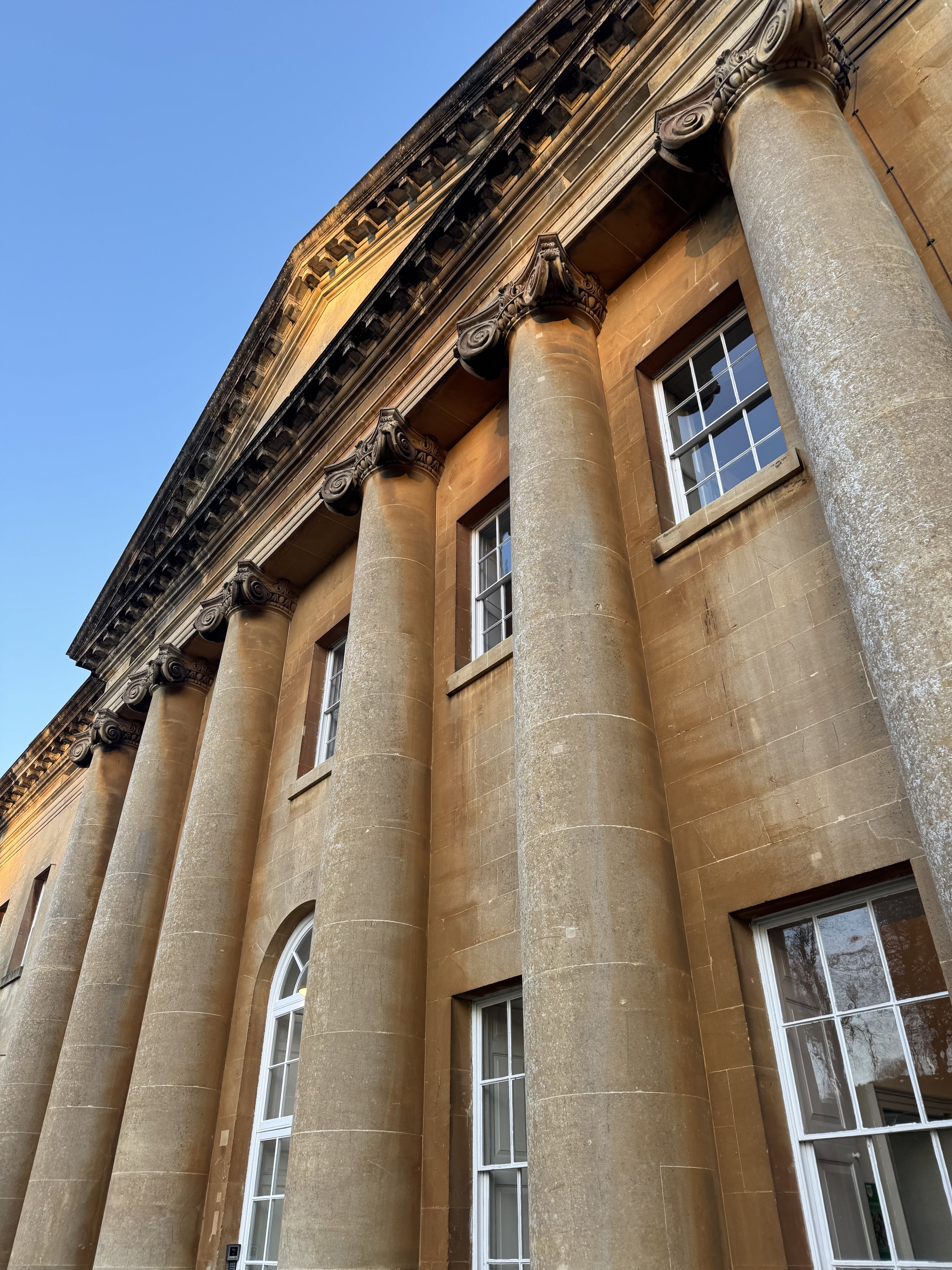 Close-up of a historic building facade with large classical columns, arched windows, and decorative molding at the top, with a clear blue sky in the background.