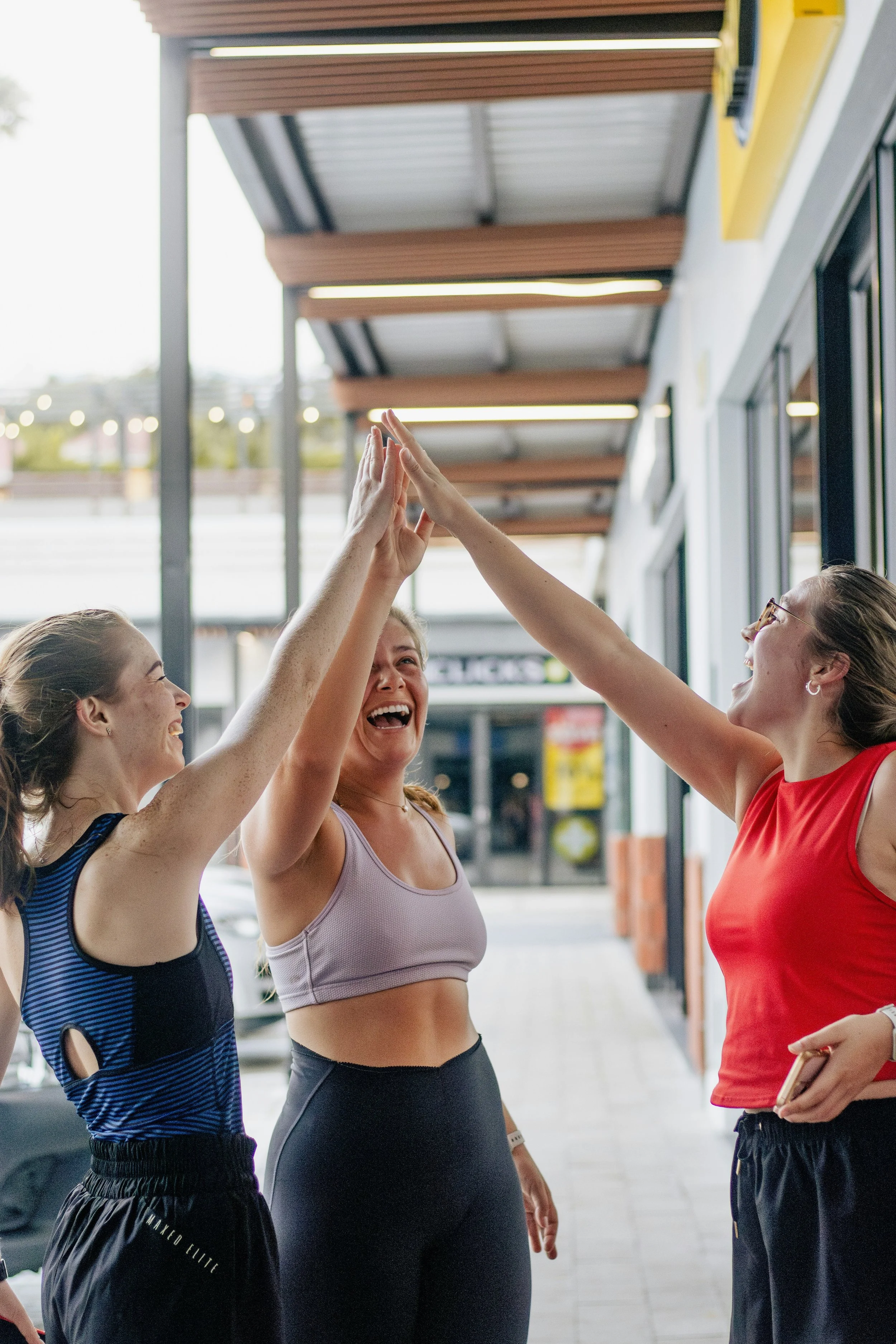 Four women in athletic clothing giving high fives outside a building with a covered walkway.
