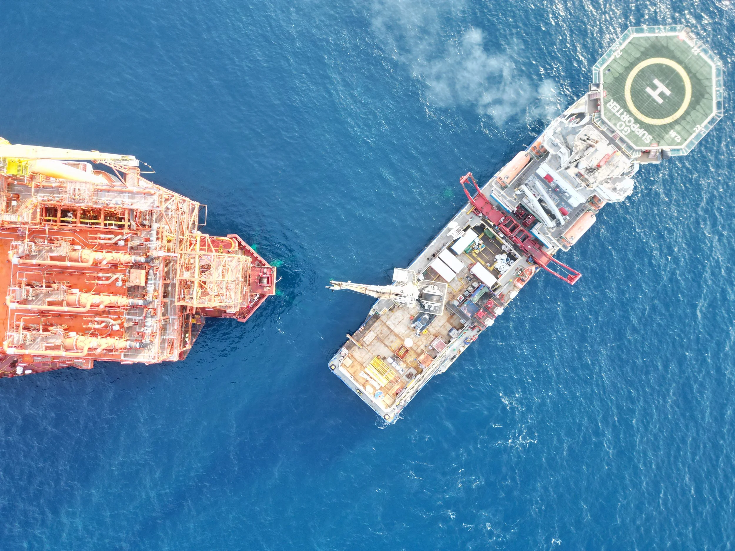 Aerial view of oil and gas platform and support vessel in the ocean.