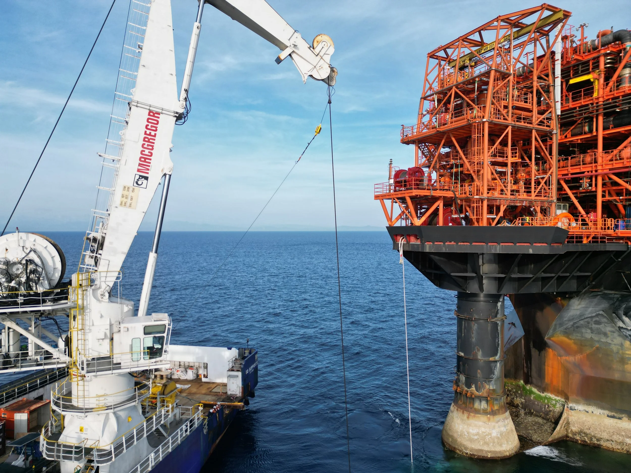 Offshore oil rig with a ships main crane working on it in the ocean under a partly cloudy sky.