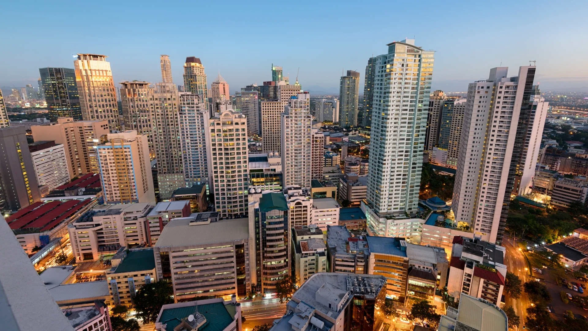City skyline at dusk with numerous tall skyscrapers illuminated by city lights.