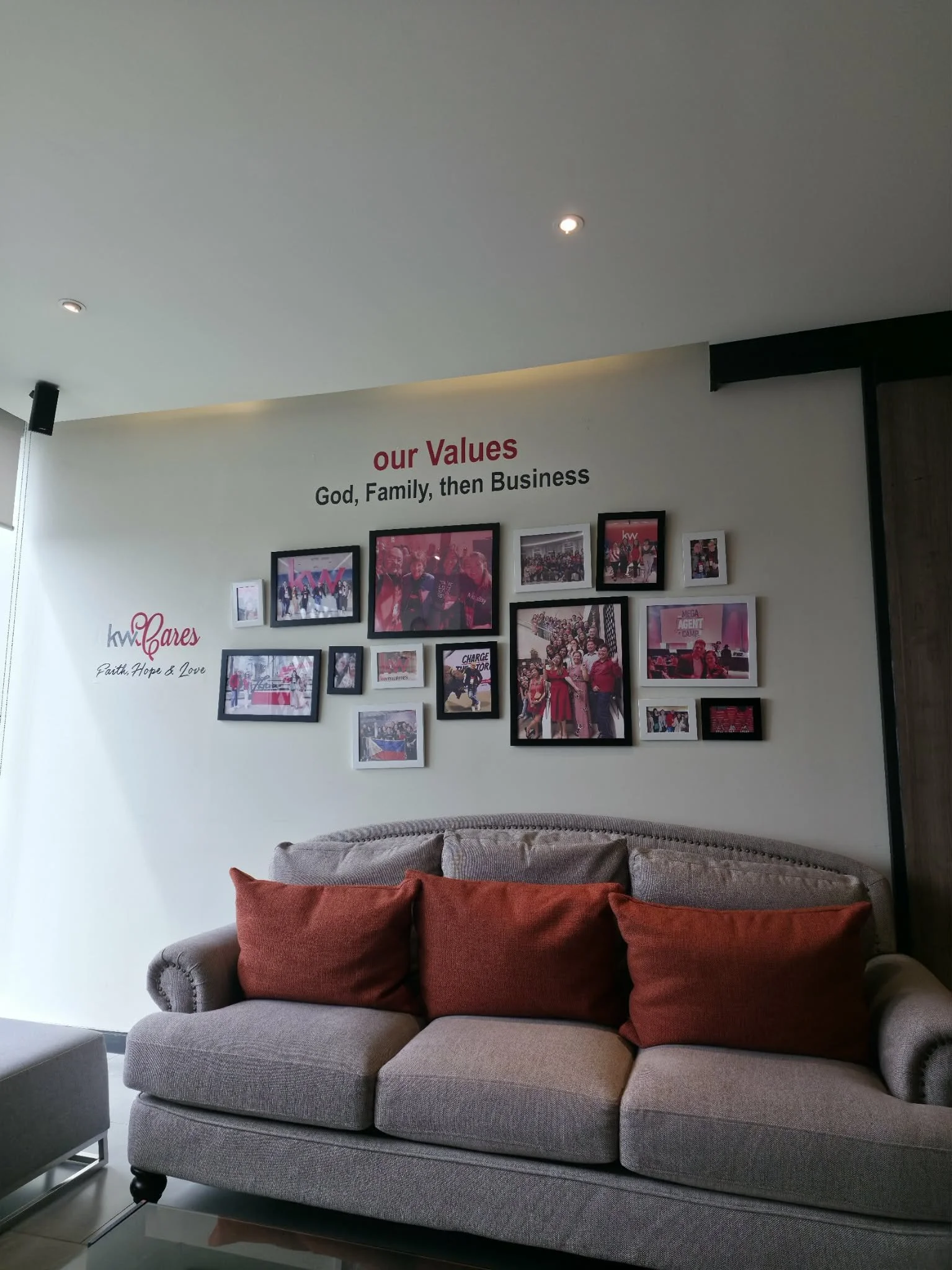 Living room with a gray sofa and three red cushions against a wall decorated with framed photographs and text about company's values and cares.