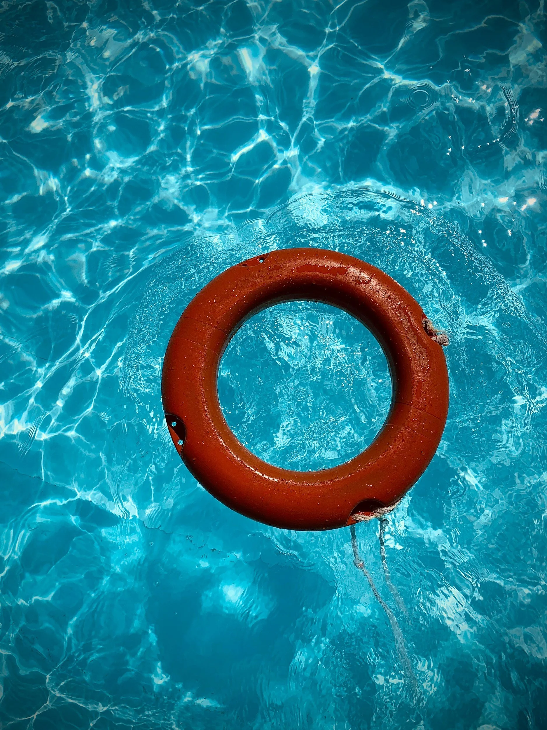 A red life preserver floating on clear blue swimming pool water.